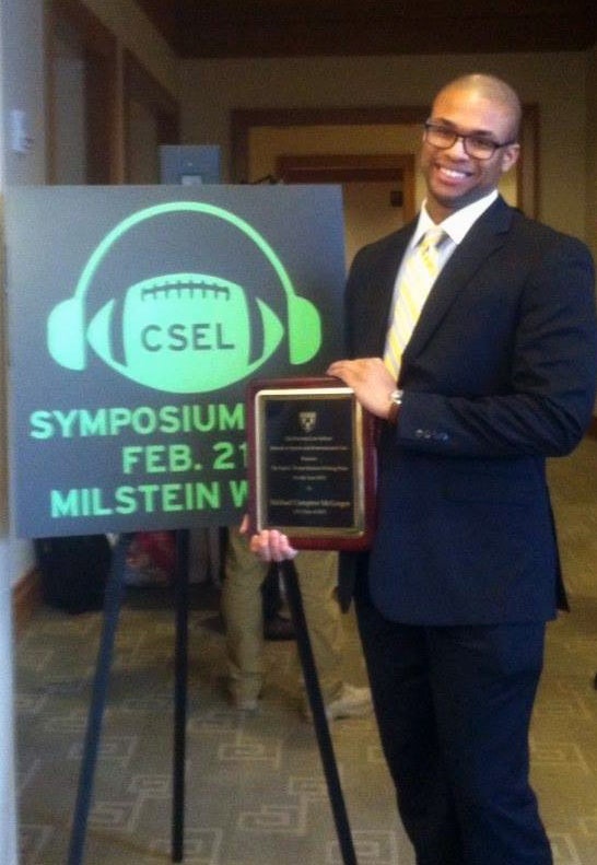 Michael McGregor holding an award near a CSEL Symposium banner