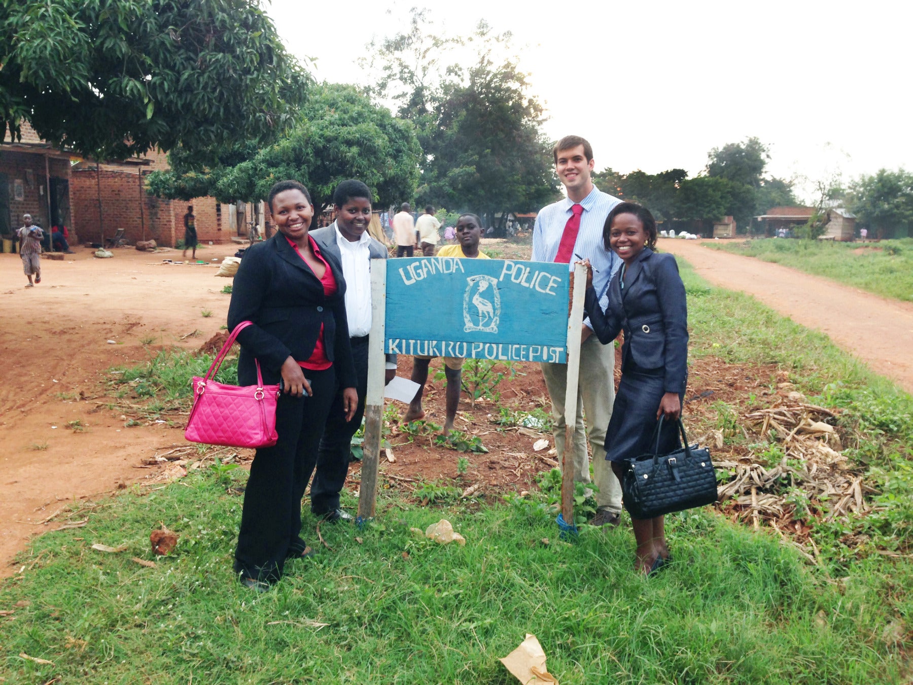 Five people posing around a sign that reads 'Uganda Police Kitukru Police Post'