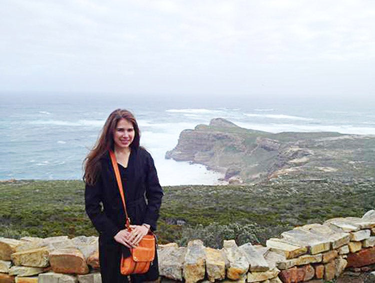 A woman posing in front of a short stone wall by the ocean
