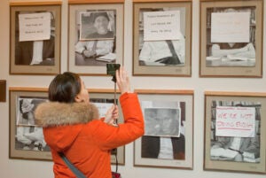 A woman in a winter coat taking a photo of some framed artifacts on the wall