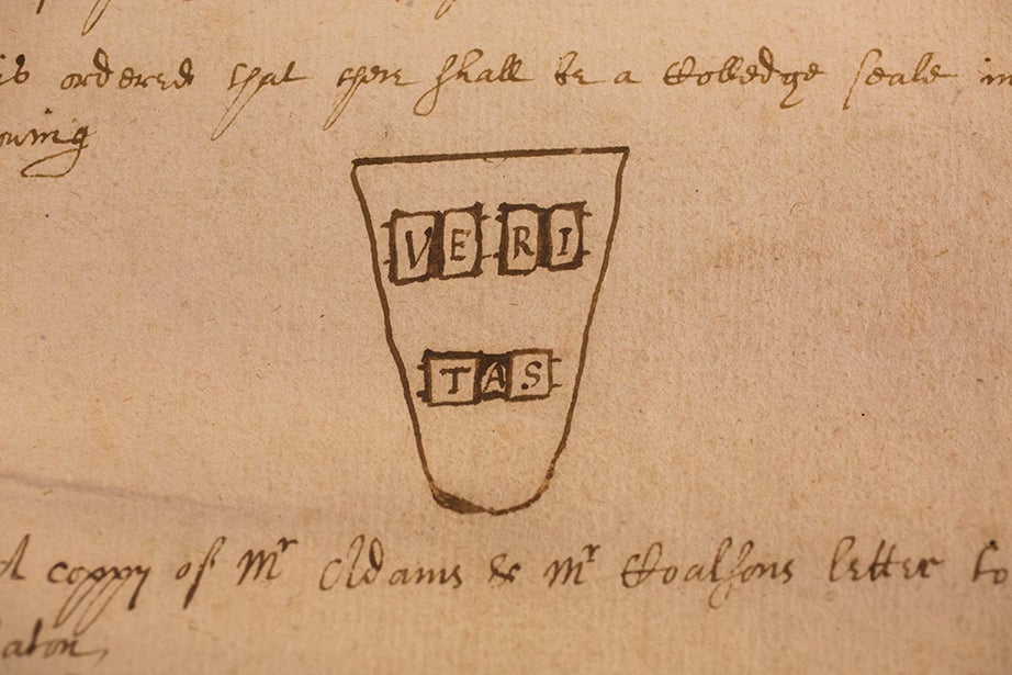 A close up of a weathered page of a book with a drawing of a shield with the words VERI TAS on it