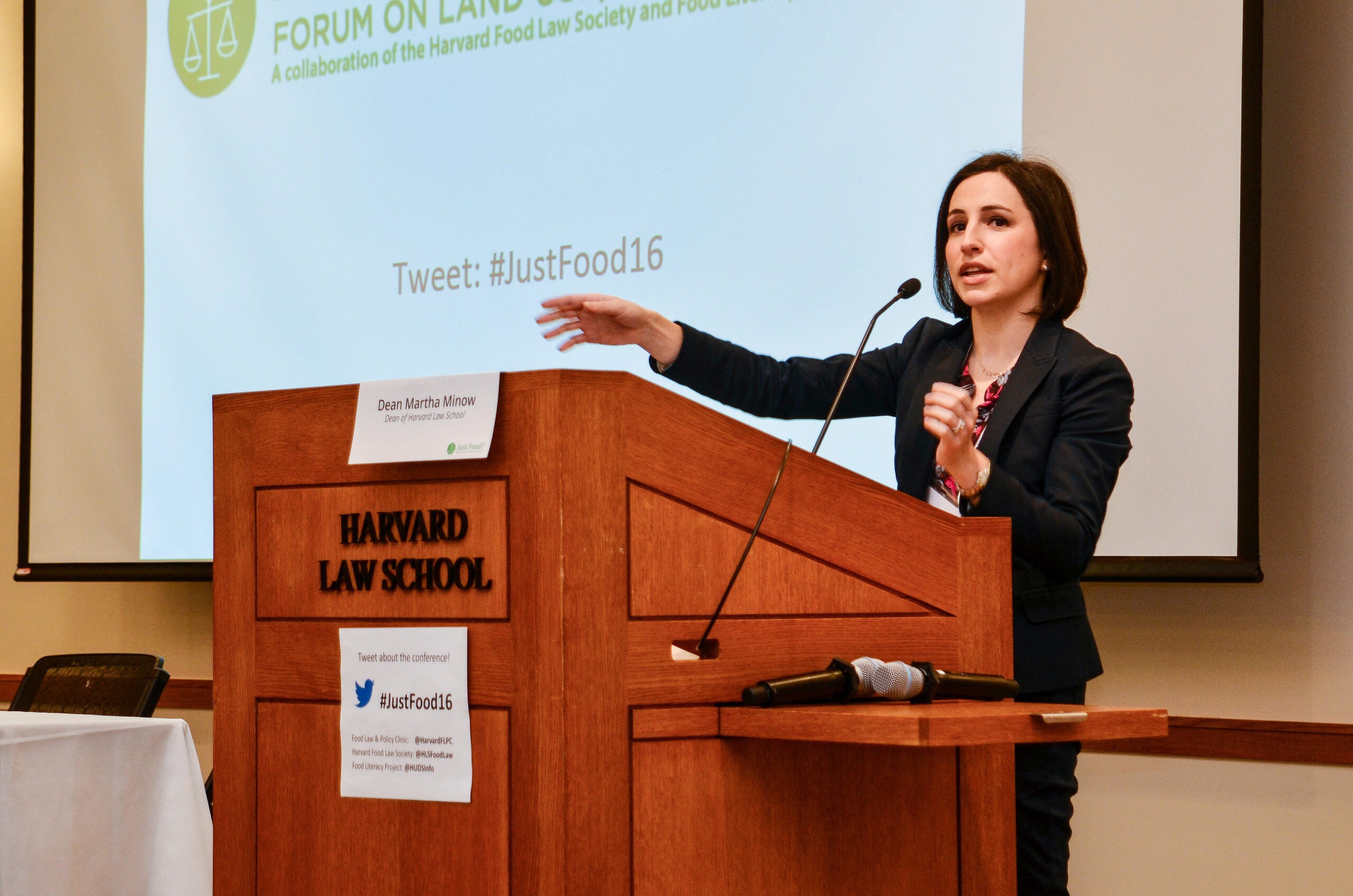 Emily Broad Leib standing at a wood podium speaking in front of a projected slide