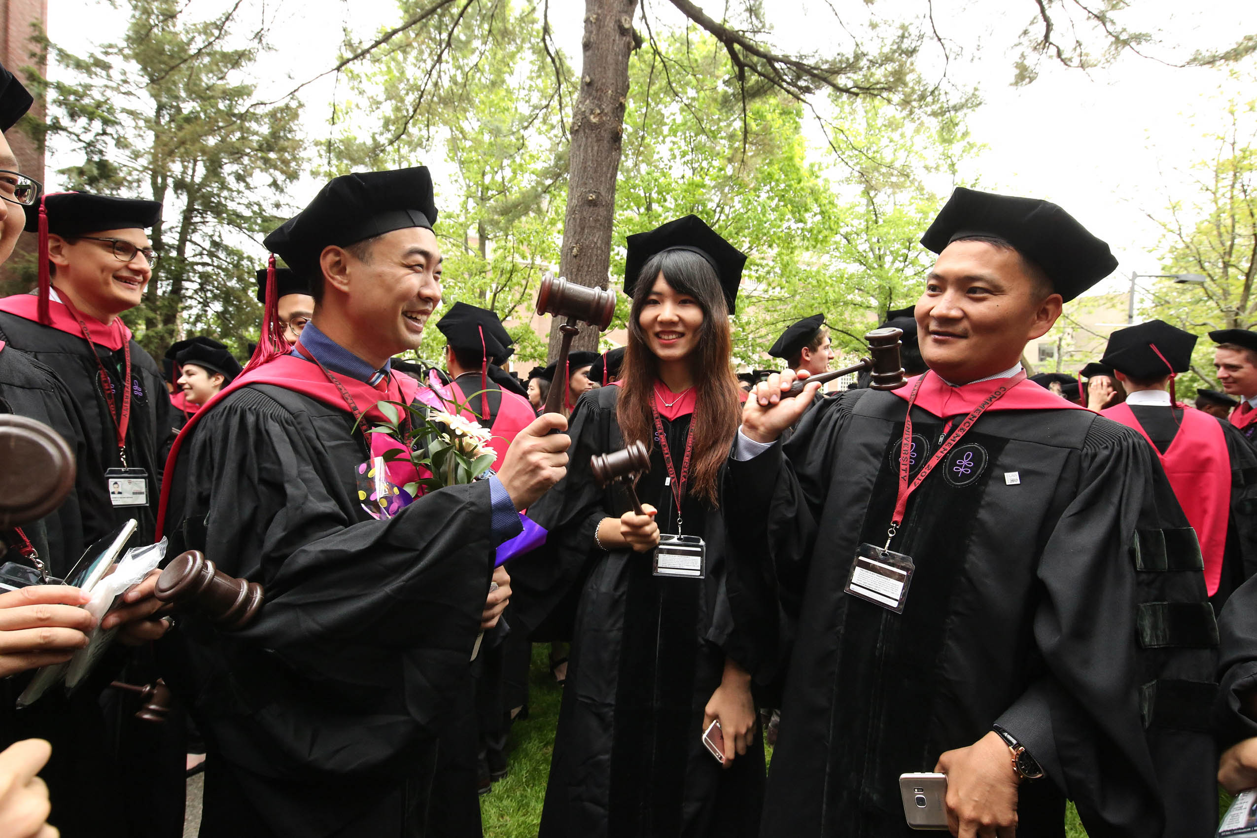 Three students in caps and gowns, holding gavels and smiling