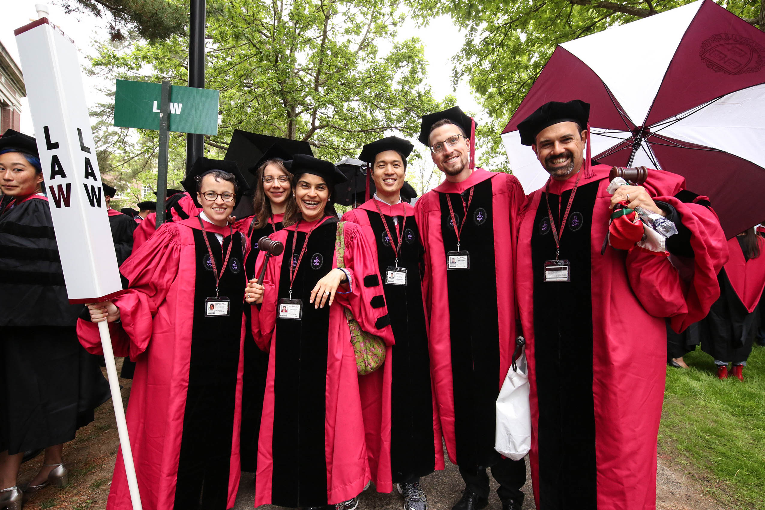 Six students in caps and gowns on Holmes Field, smiling