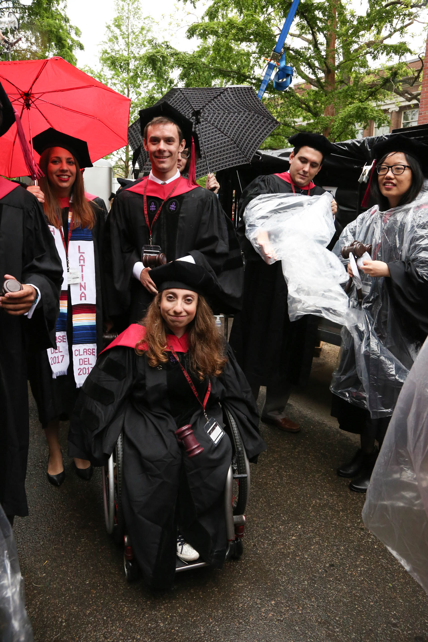 Five students in caps and gowns, standing under umbrellas and smiling