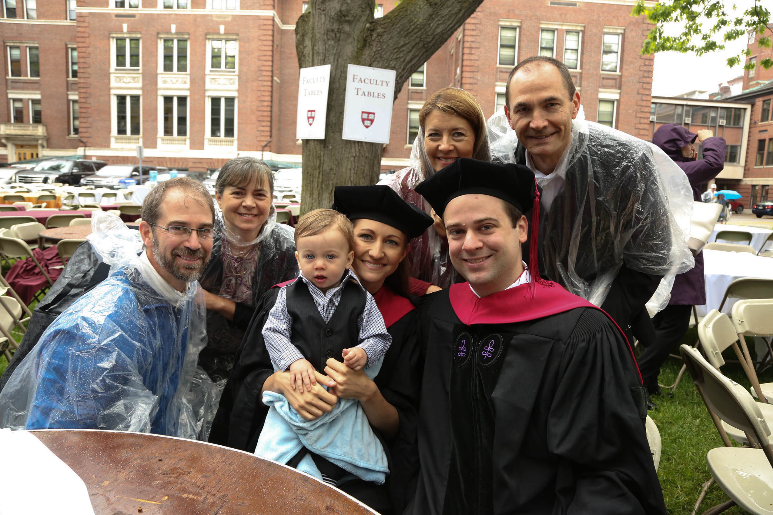 Three men, three women, and a baby sitting on Holmes Field, smiling