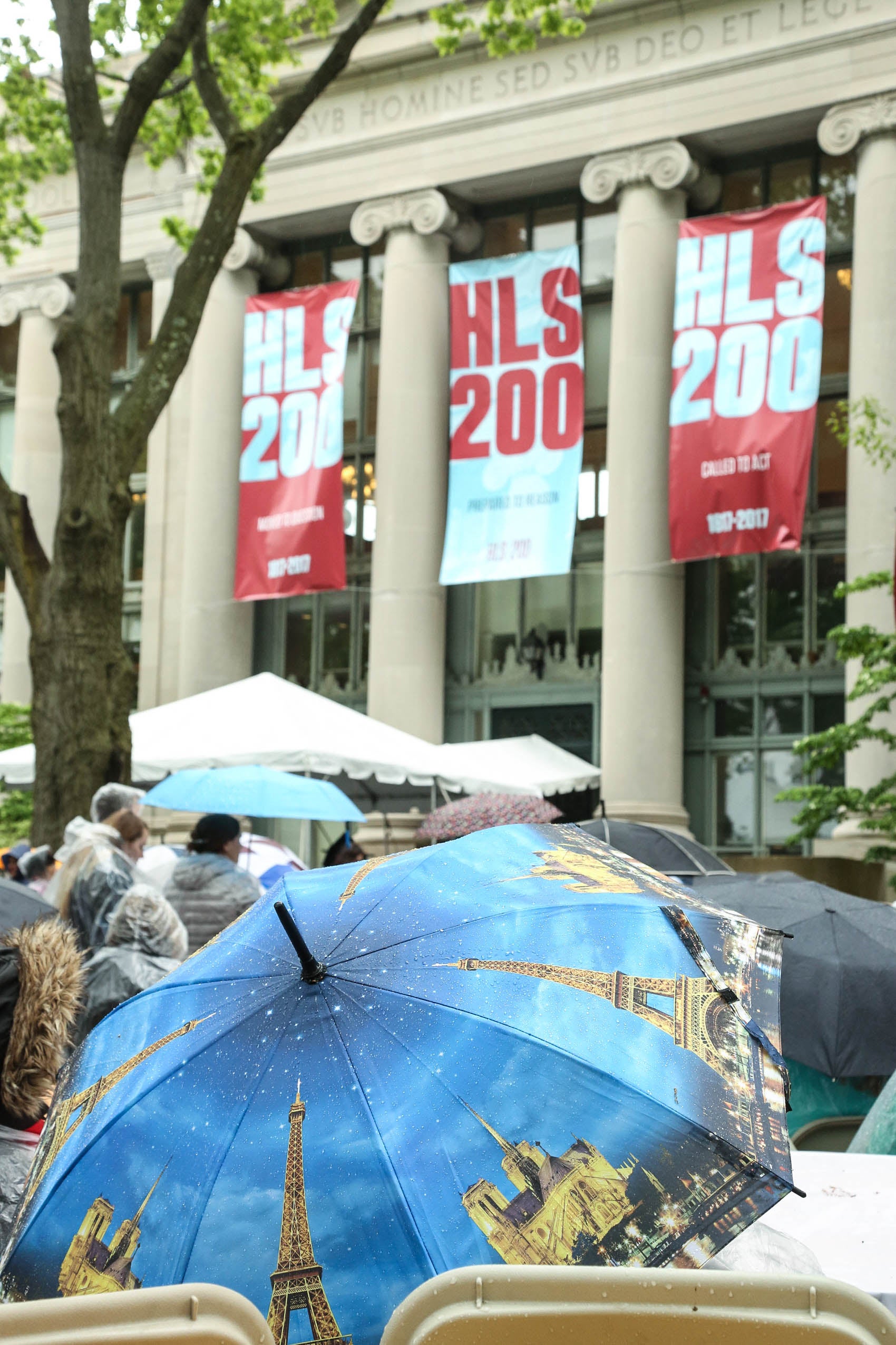 People seated on Holmes Field in front of Langdell Hall, covered by umbrellas