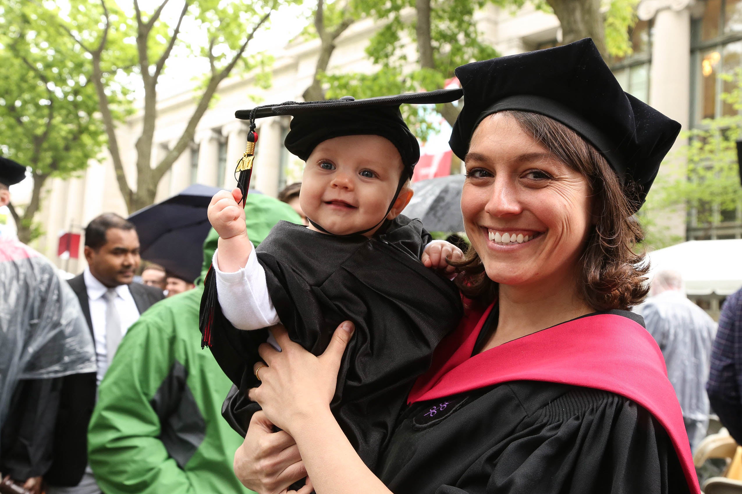 A woman in cap and gown, smiling and holding a baby in cap and gown