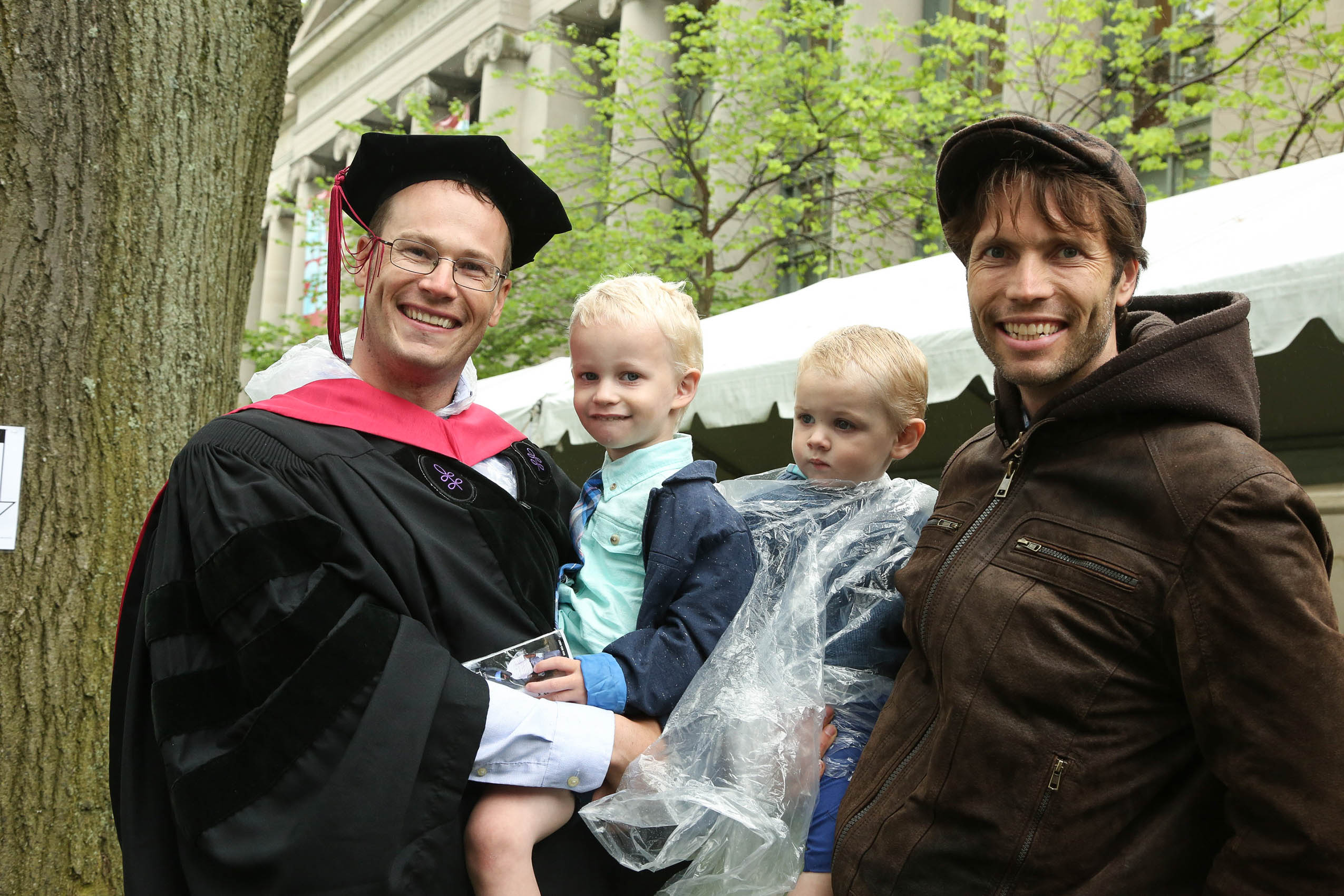 Two men and two babies standing on Holmes Field in front of Langdell Hall, smiling