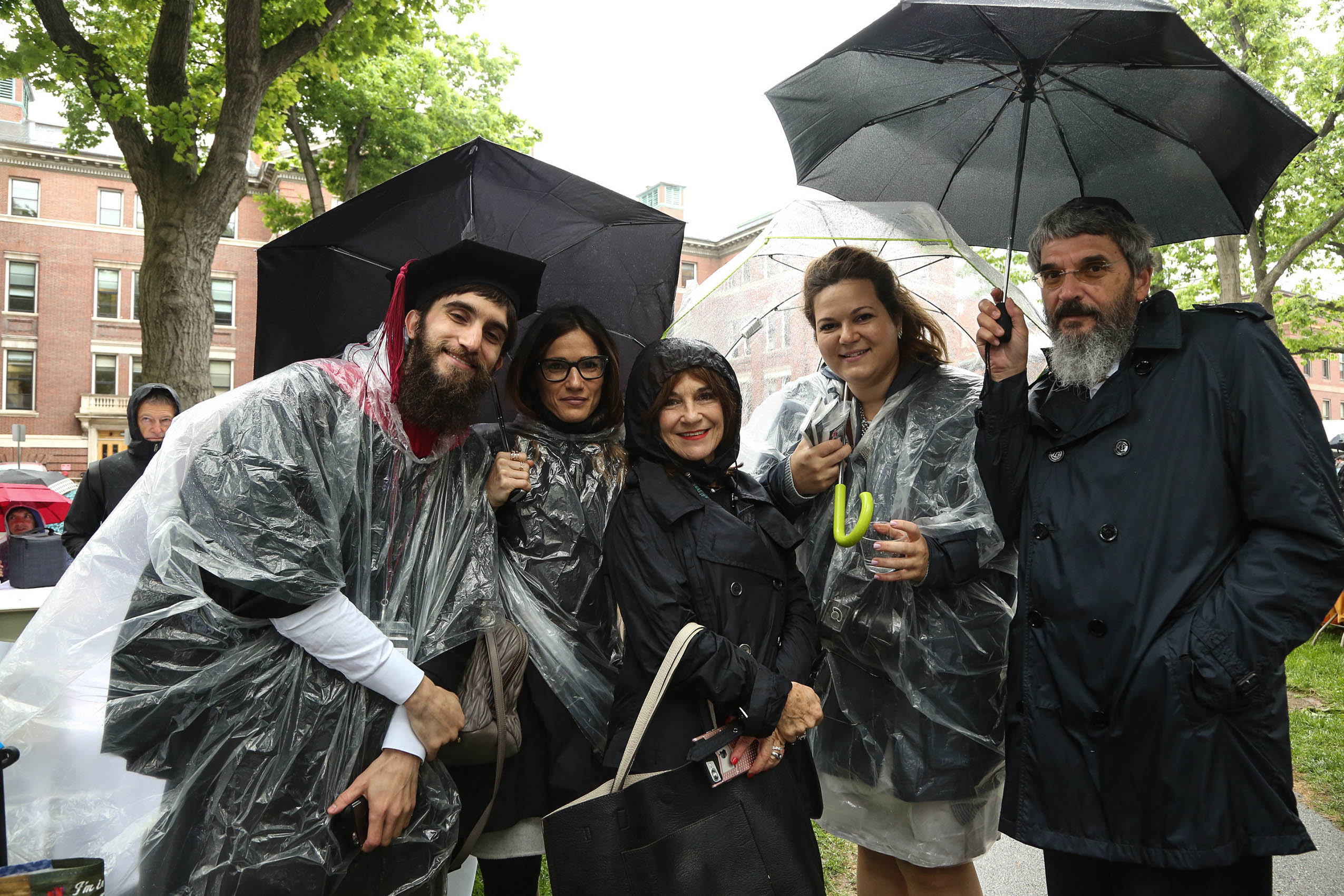 A group of three women and two men standing on Holmes field in ponchos with umbrellas, smiling