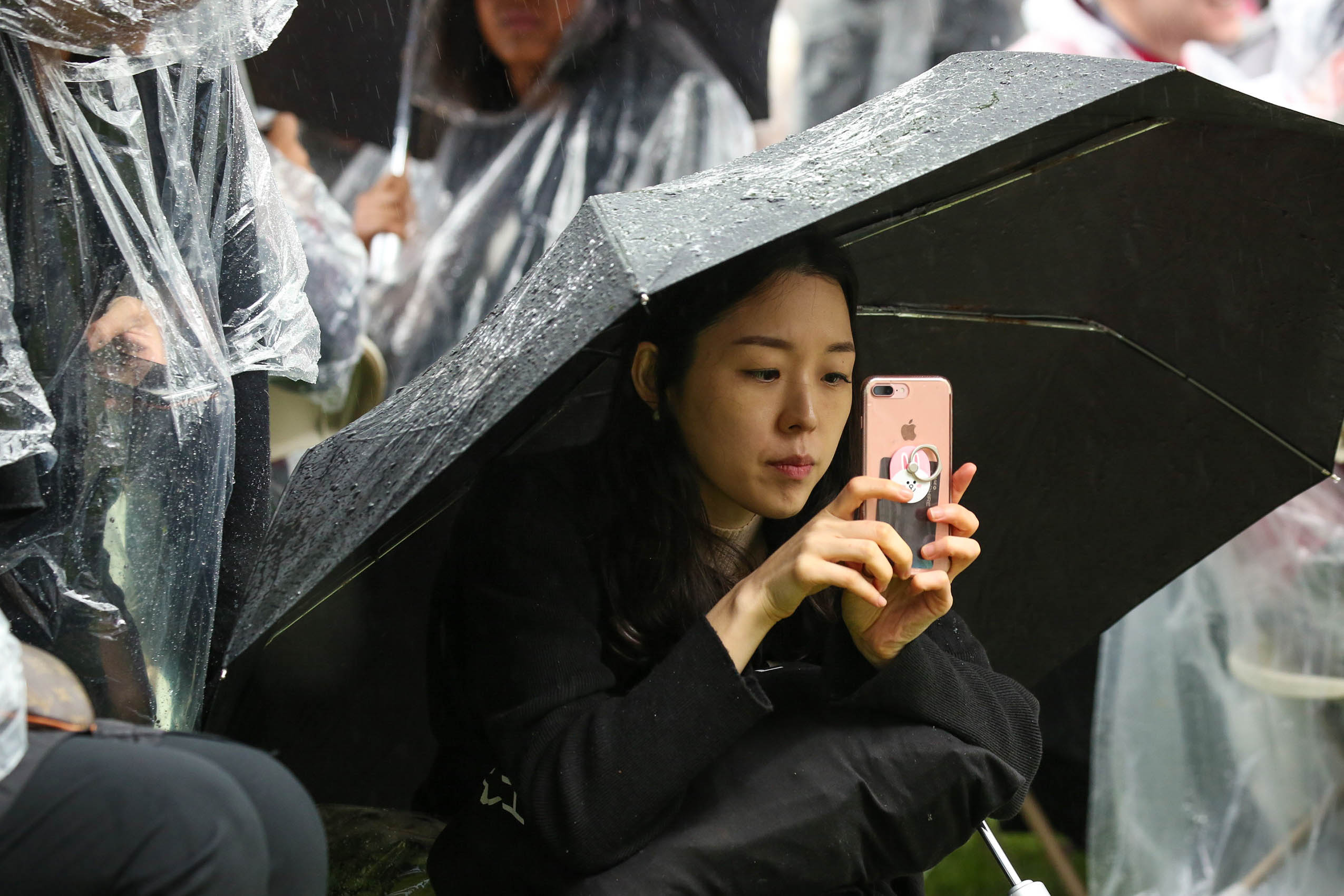 A woman taking a photo on her phone from under an umbrella