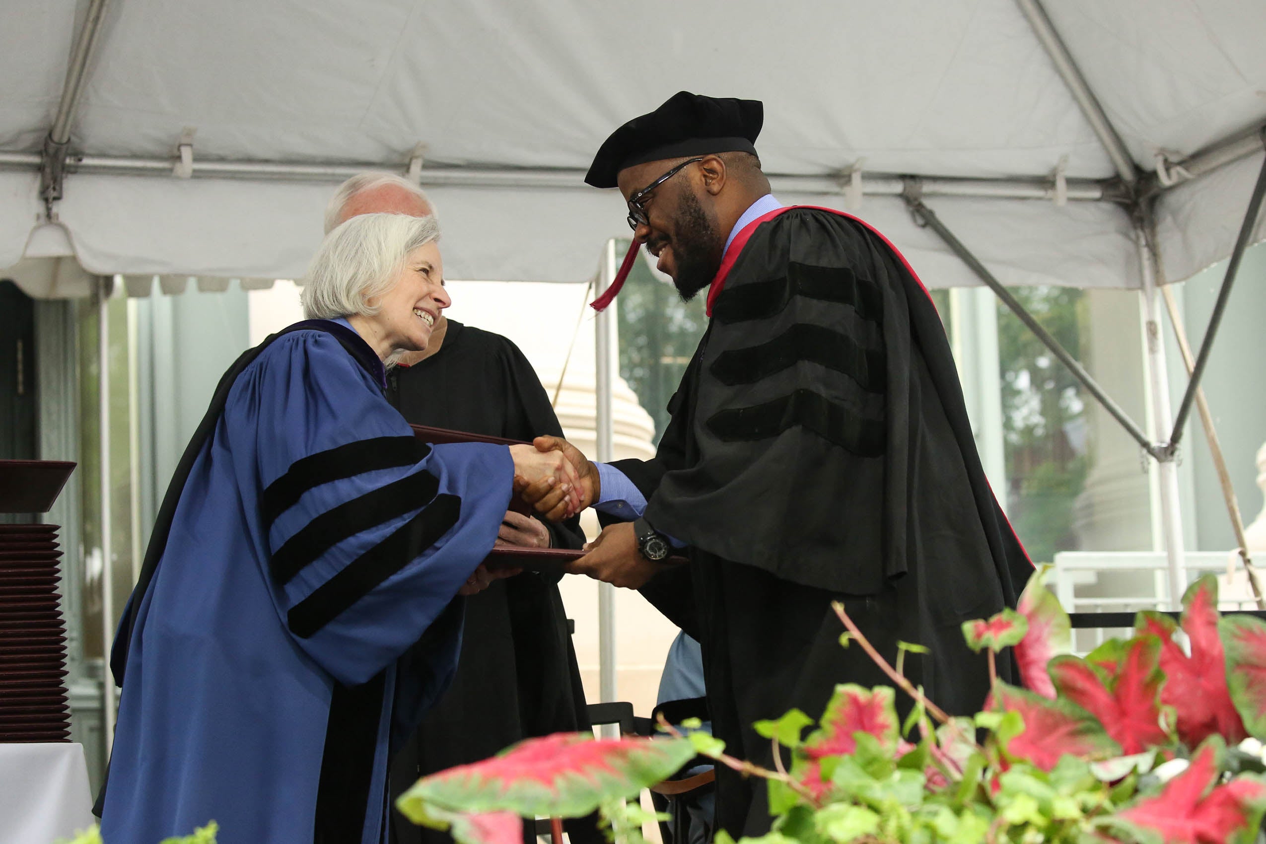 A man and woman in cap and gown, standing on a stage shaking hands