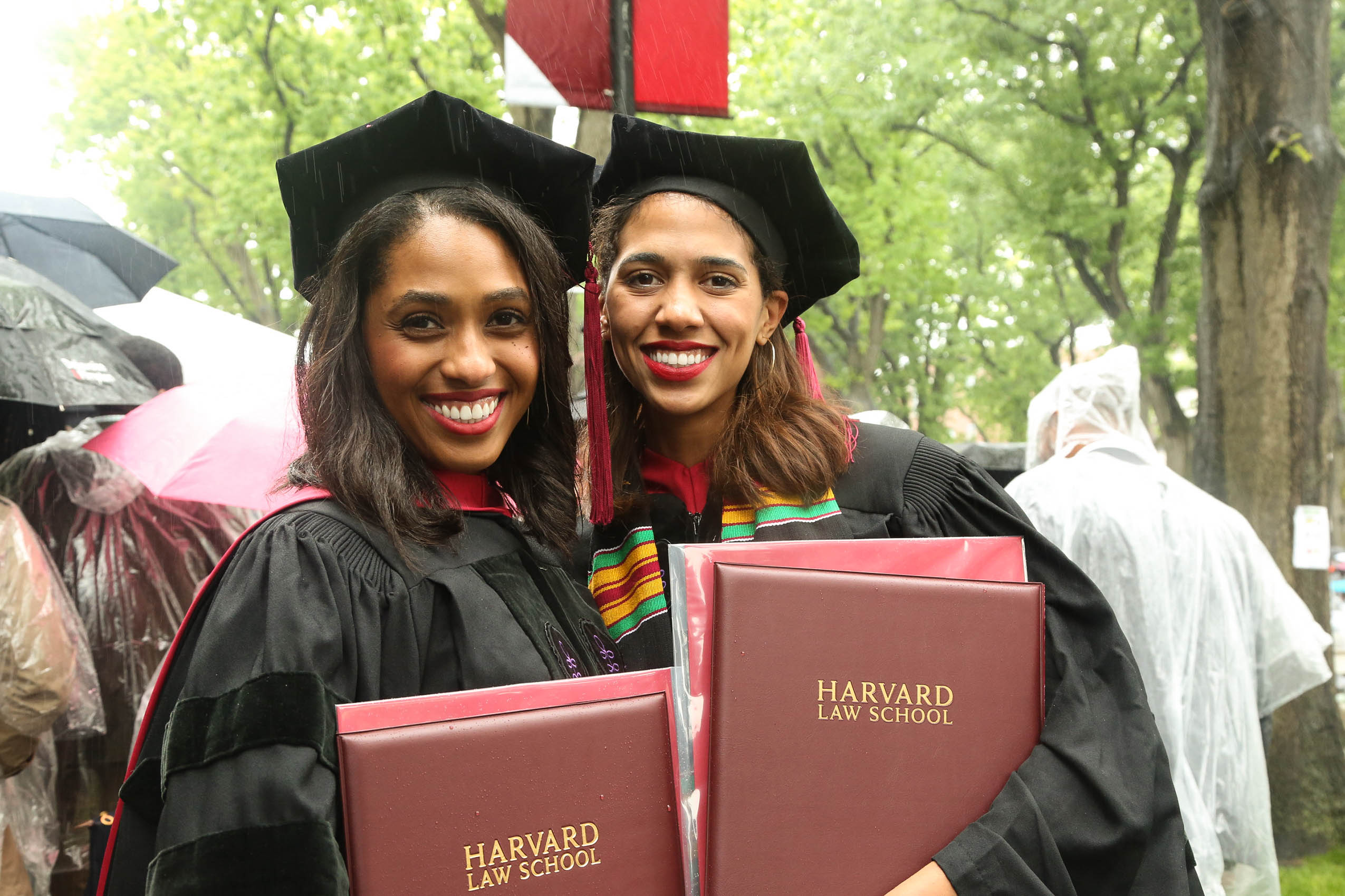 Two women in cap and gown holding their degrees, smiling