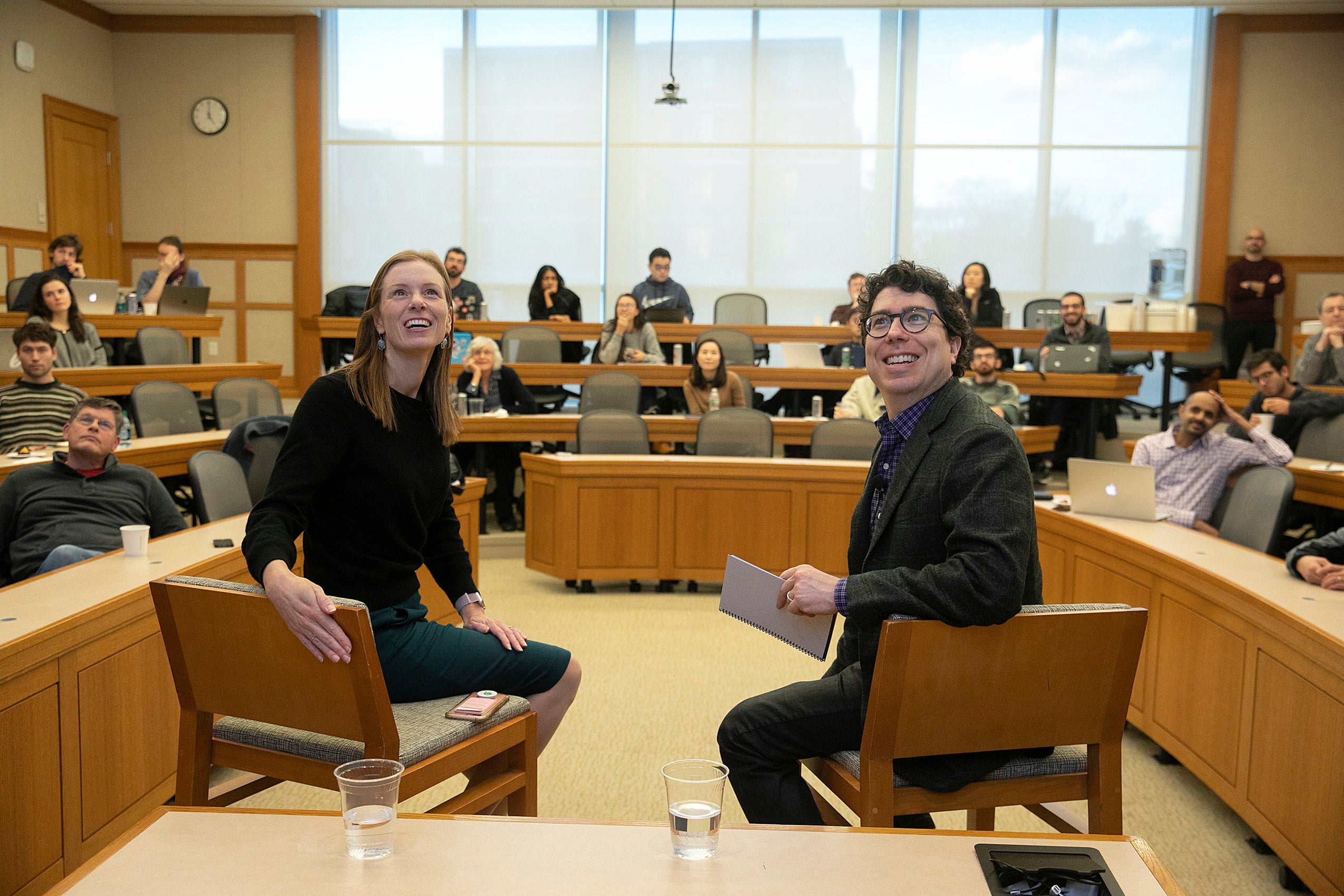 Monika Bickert and Jonathan Zittrain seated at the front of a classroom smiling and looking up at a screen