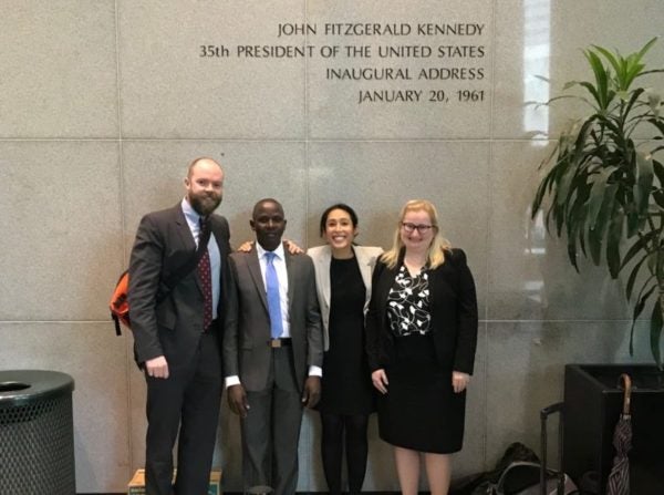 Phil Torrey, Abraham, Cindy Zapata, and Alicia Coneys, J.D. '19 stand in front of a wall reading 'John Fitzgerald Kennedy 35th President of the United States Inaugural Address January 20, 1961'