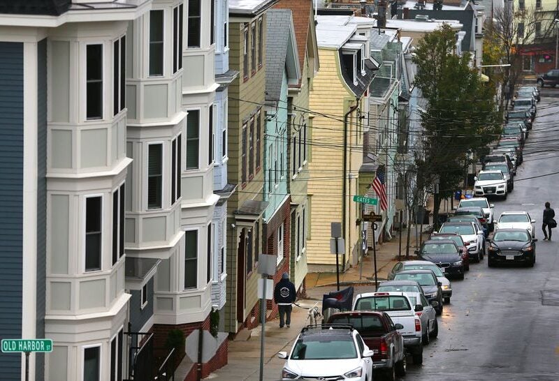 Photo angled down a street in Boston showing town houses and parked cars. Street signs for Gates St and Old Harbor St are visible, along with two residents walking.