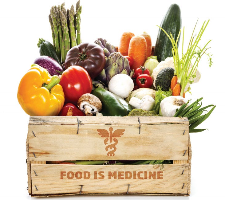 A wooden box with a caduceus and the inscription: 'Food is Medicine' holds fresh produce