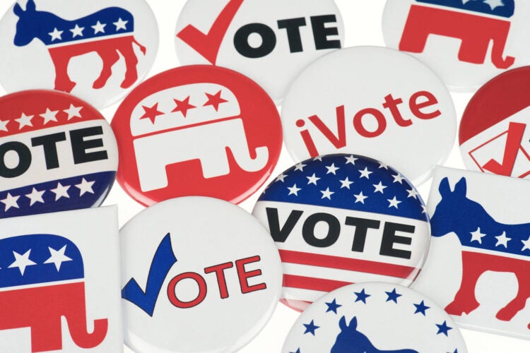 A collection of voting pins in red, white, and blue on a white background. Some read 'VOTE' or 'iVOTE'