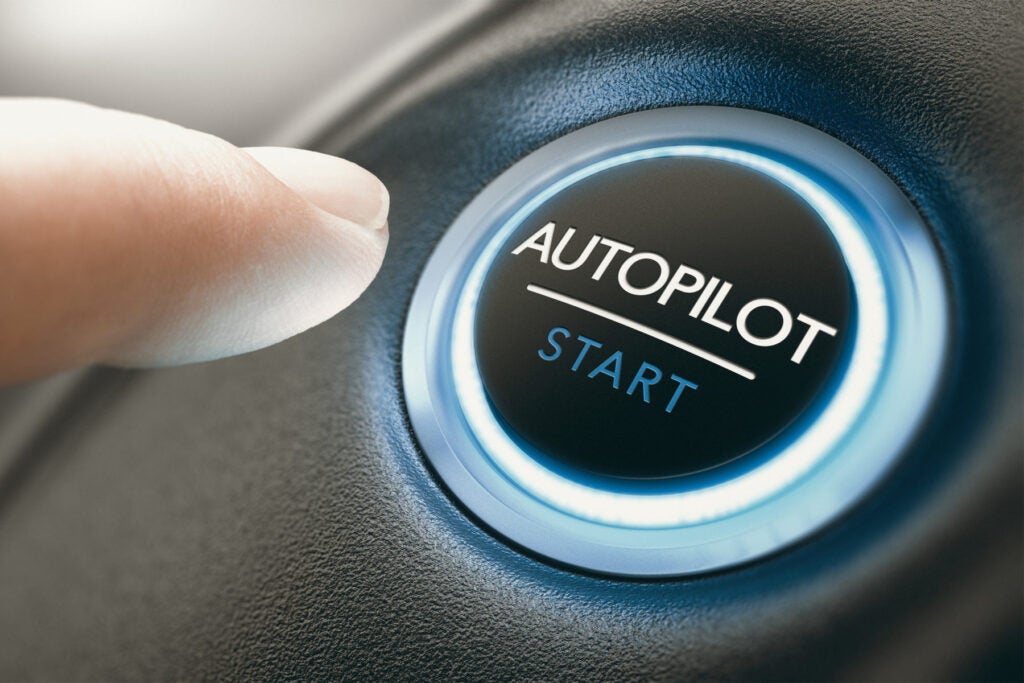 FINGER PRESSING AN AUTOPILOT BUTTON IN A SELF DRIVING CAR. COMPOSITE IMAGE BETWEEN A HAND PHOTOGRAPHY AND A 3D BACKGROUND.