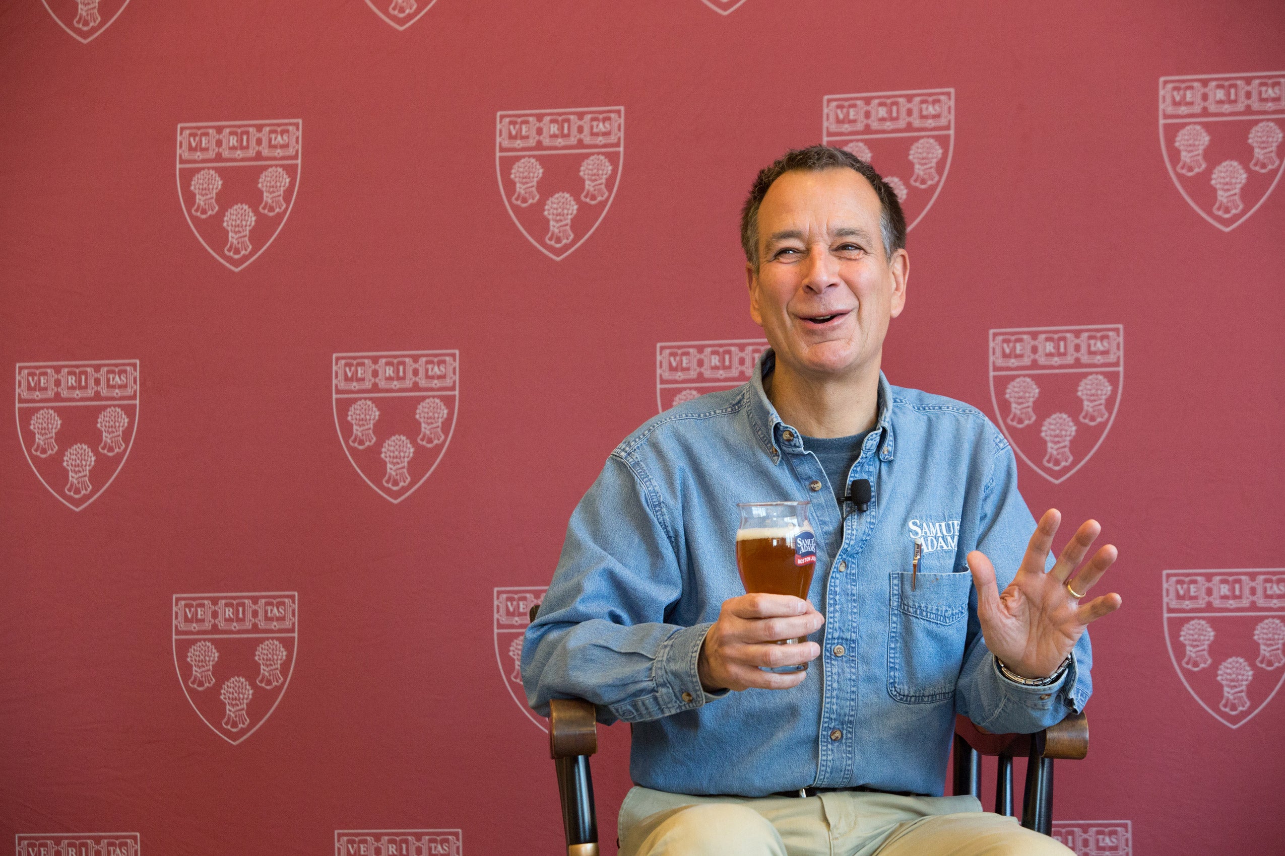 Jim Koch speaking against a Harvard backdrop with a glass of beer in his hand