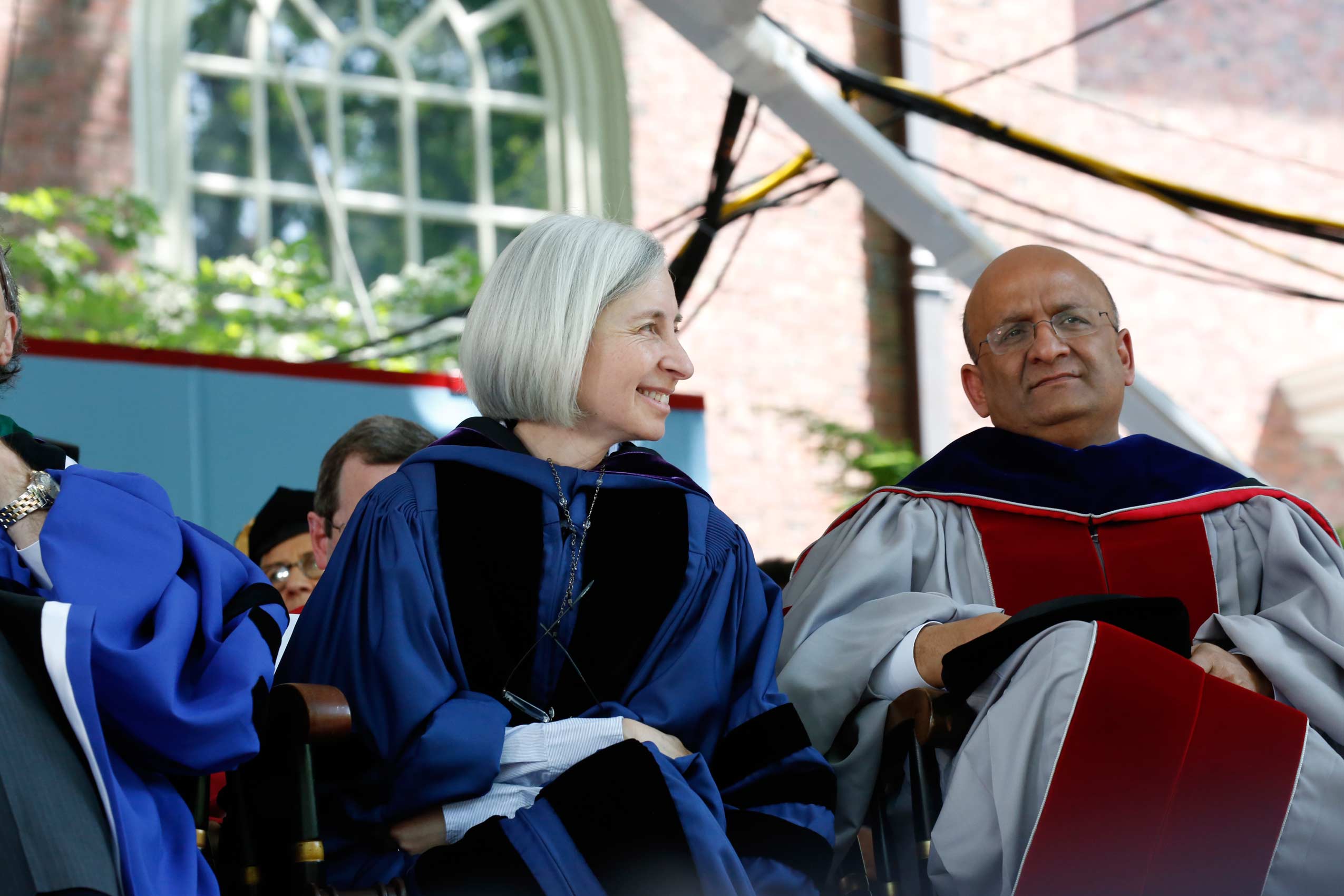 Dean Martha Minow wearing blue gown and smiling with another man wearing a silver and red gown