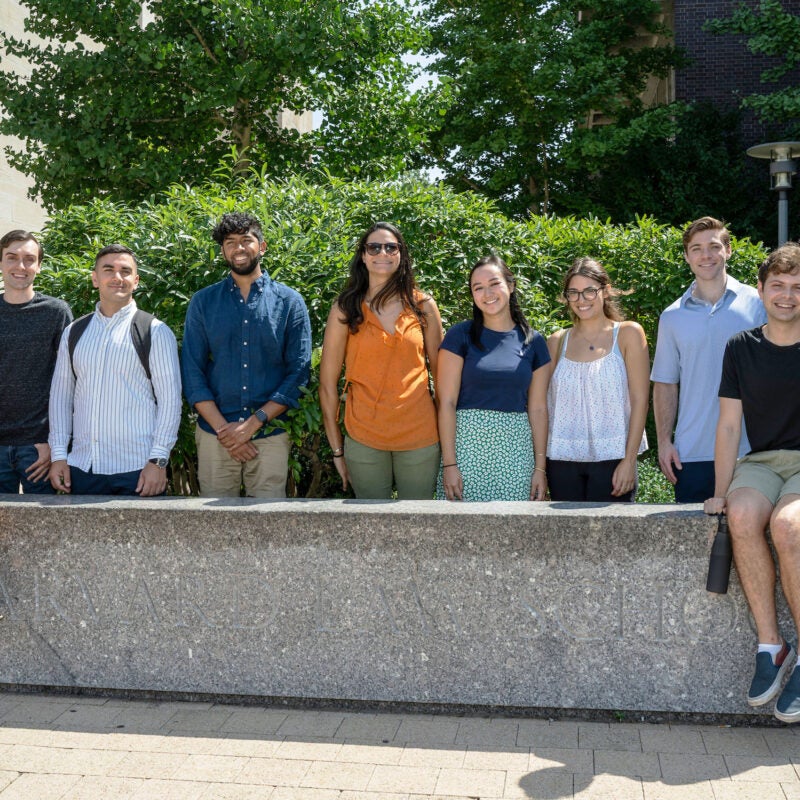 A group of ten students pose outside at granite bench on the Harvard Law School campus.