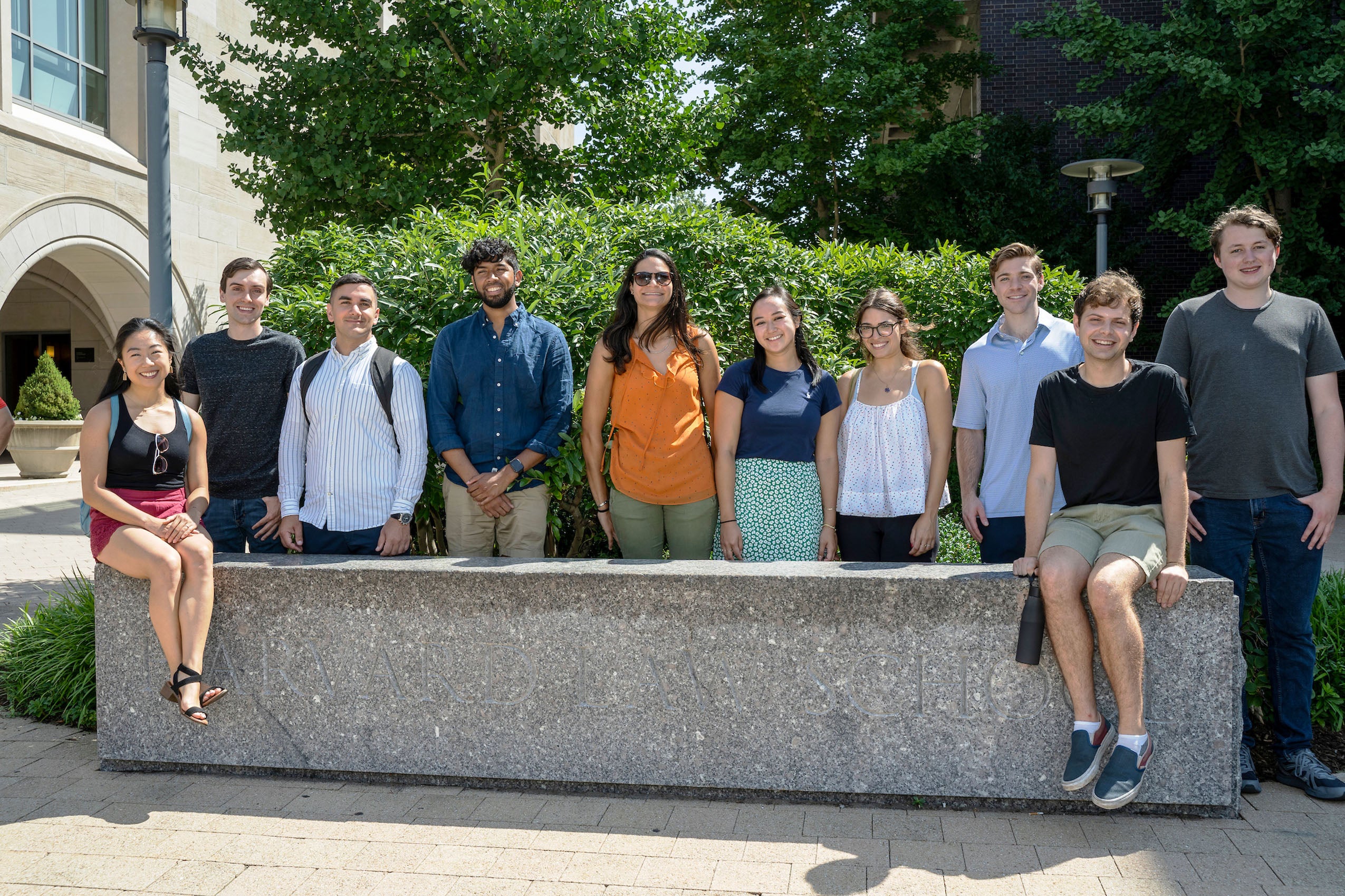 A group of ten students pose outside at granite bench on the Harvard Law School campus.
