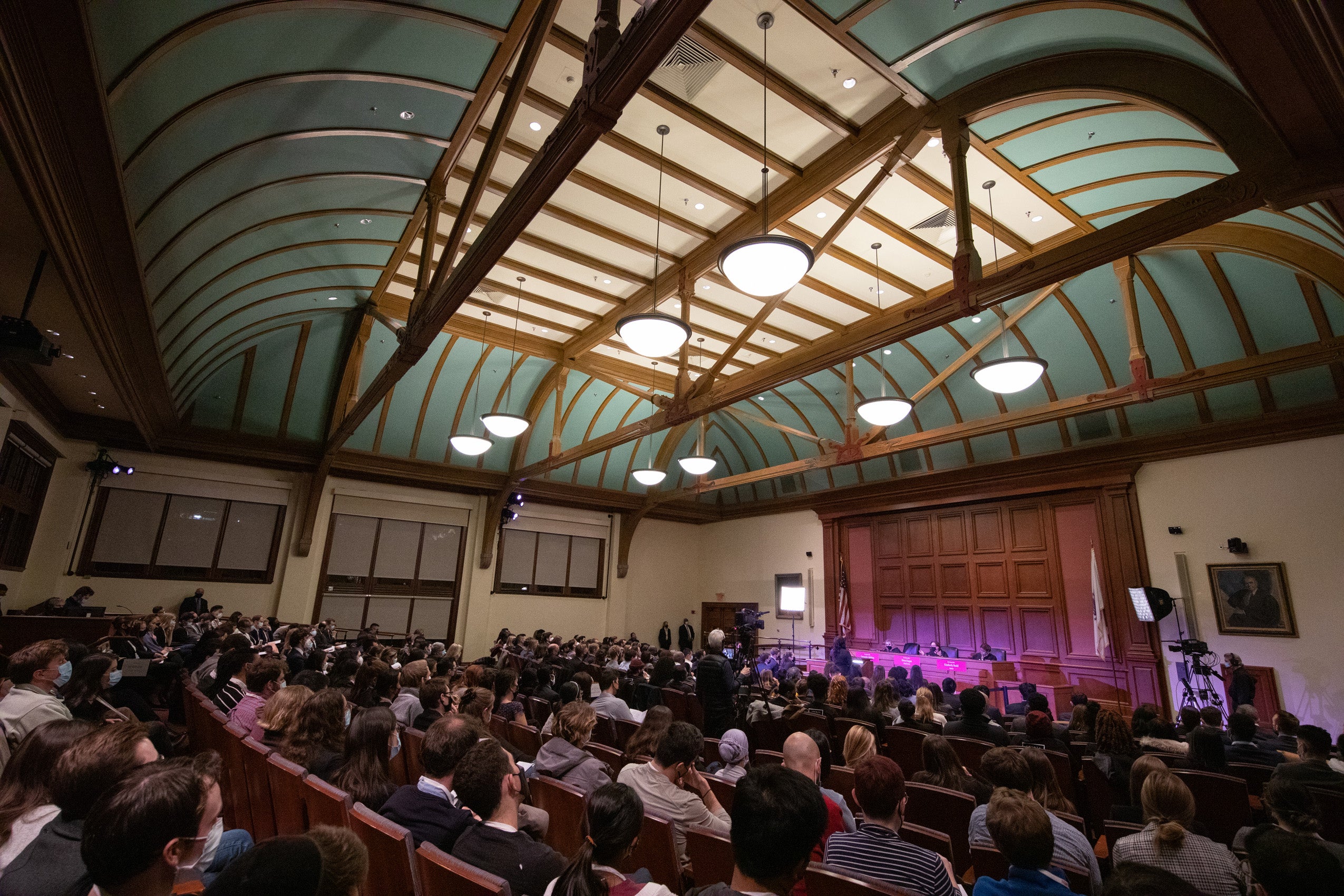 Wide view of a room with a panel of judges in the front and a large audience