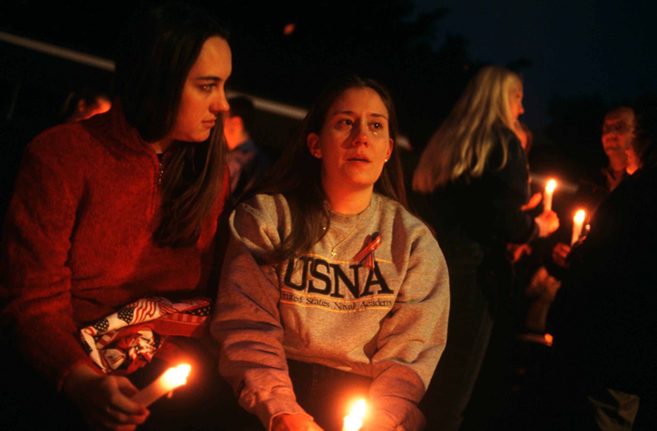 Two female students --one shedding tears—sit among members of the campus community holding lit candles at night