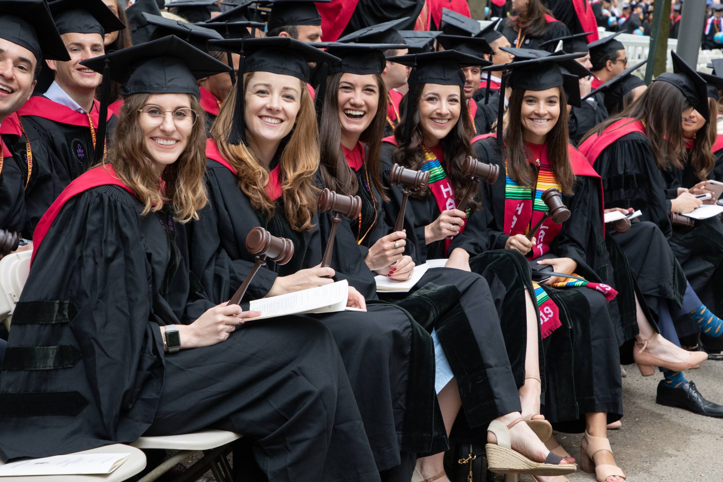 Several graduates in caps and gowns smile together holding HLS gavels