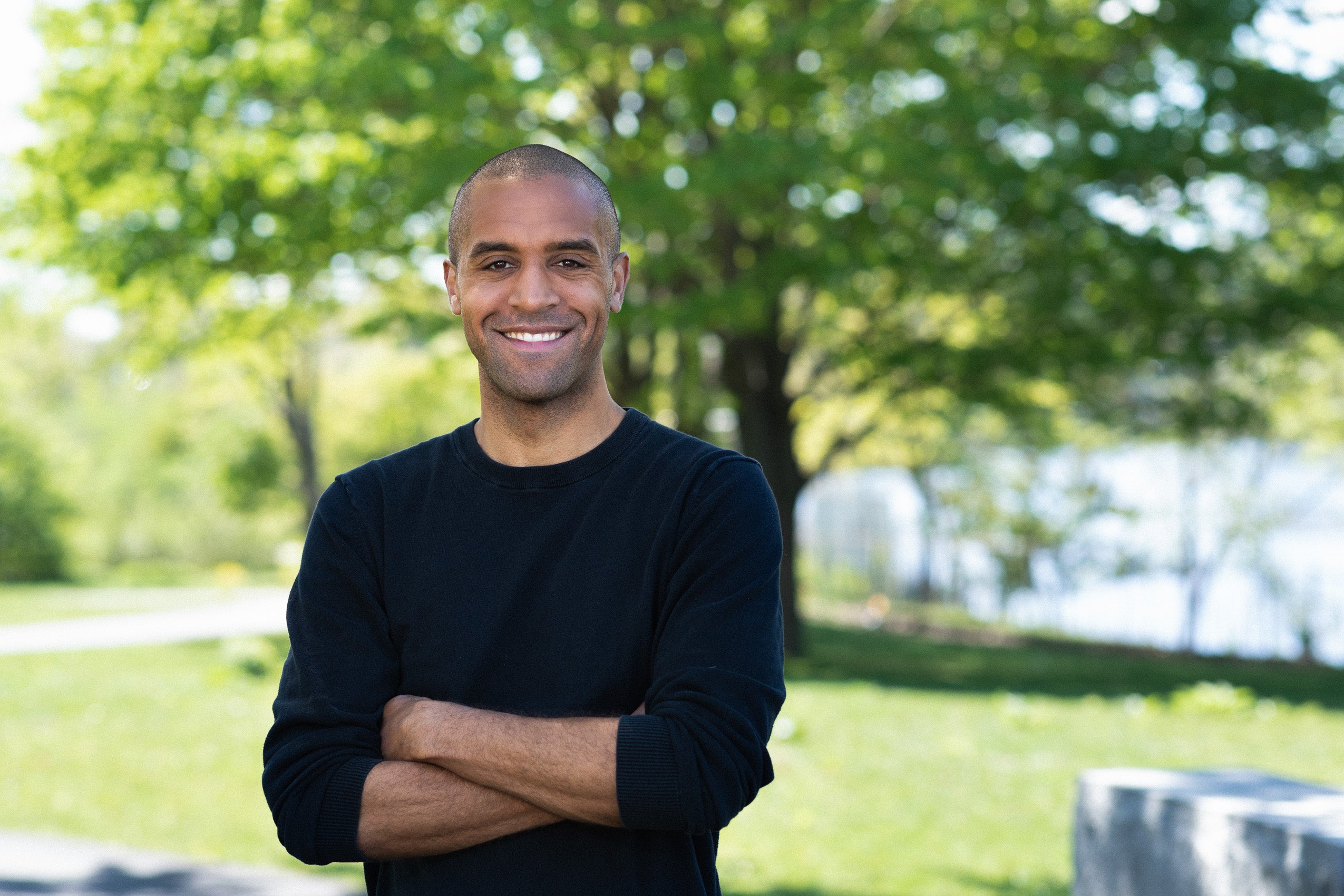 Man in a black sweater standing in front of a tree.