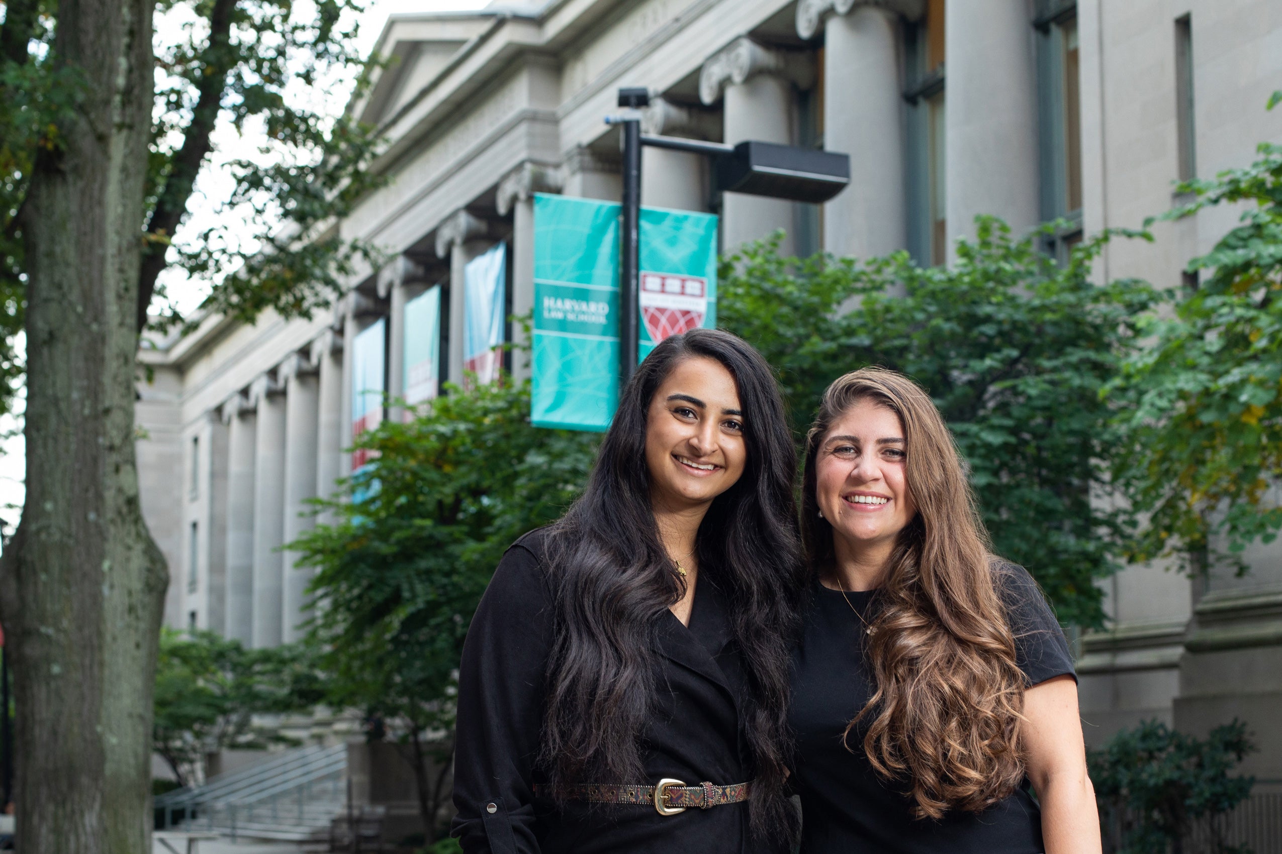 Two women in black dresses stand in front of a building on the Harvard Law School campus.