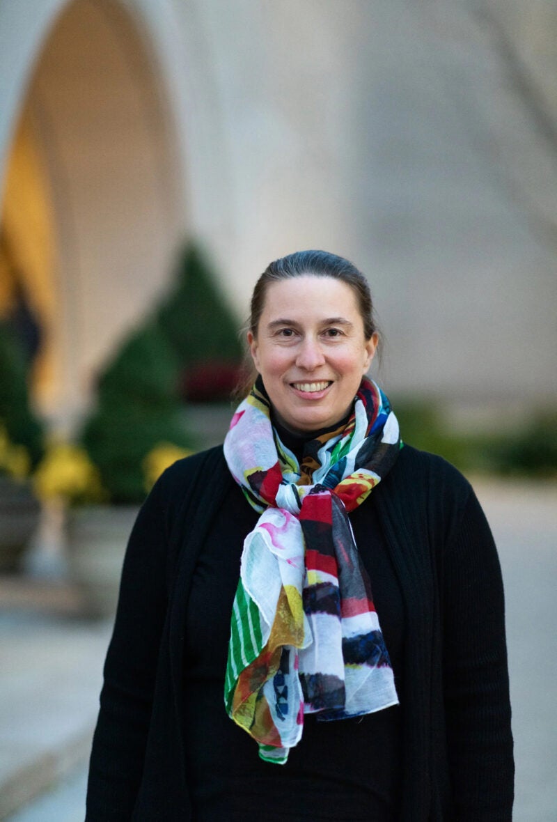A woman in a colorful scarf stands in front of a building on the Harvard Law School campus.