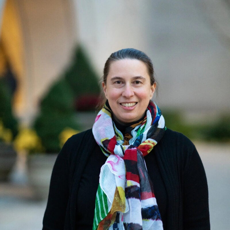 A woman in a colorful scarf stands in front of a building on the Harvard Law School campus.