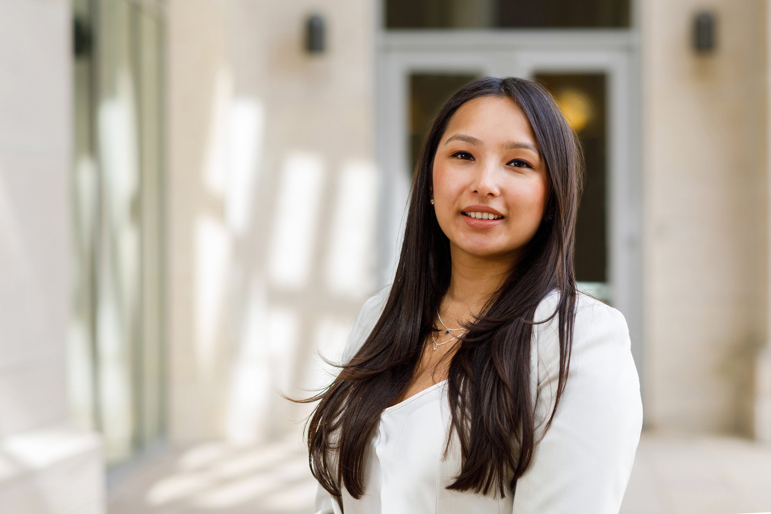 A woman in a white blazer stands in front of a doorway on the Harvard Law School campus.