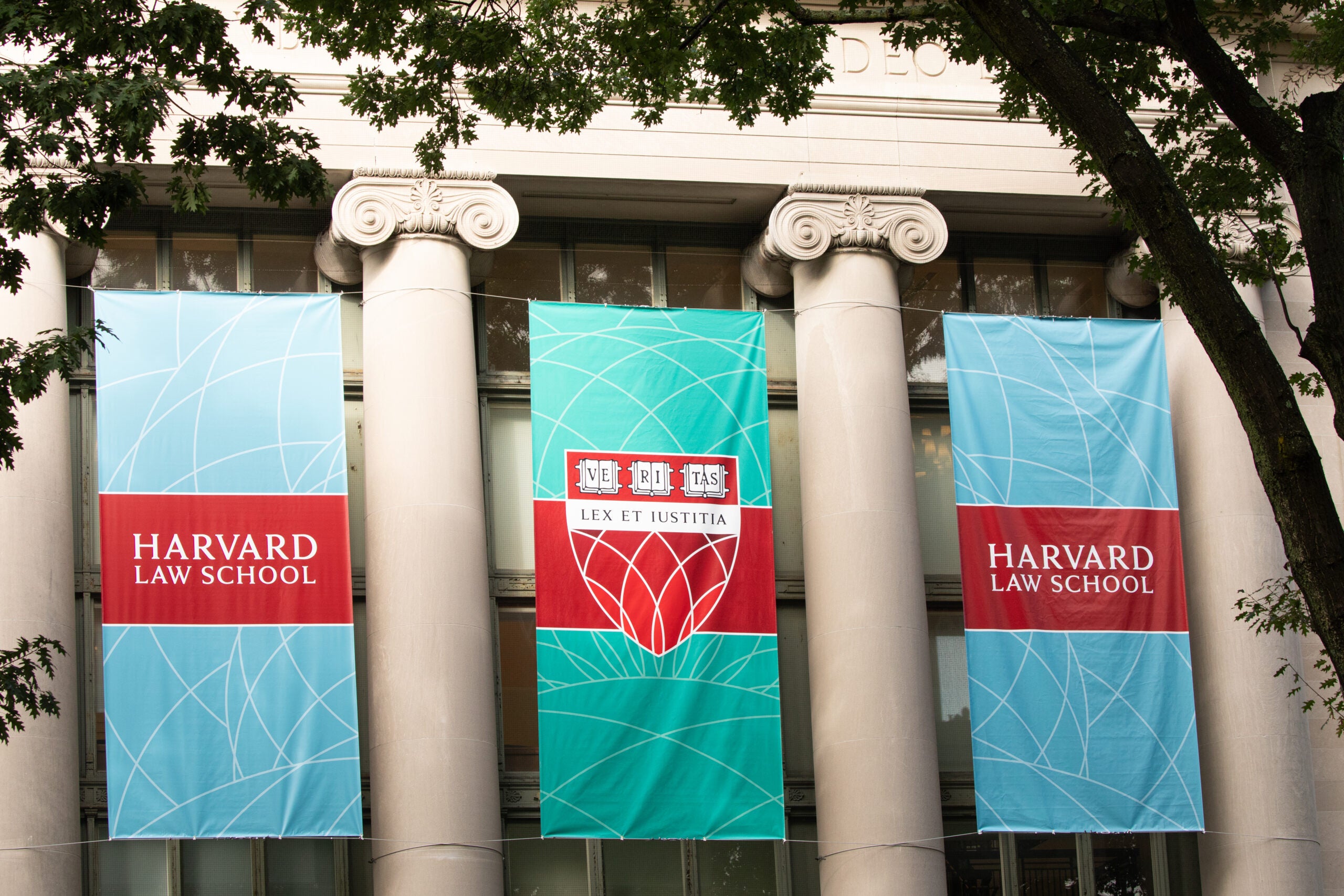 Three banners hanging outside between columns on Langdell Hall. Two read Harvard Law School. Middle one reads Veritas and Lex Et Iustitia.