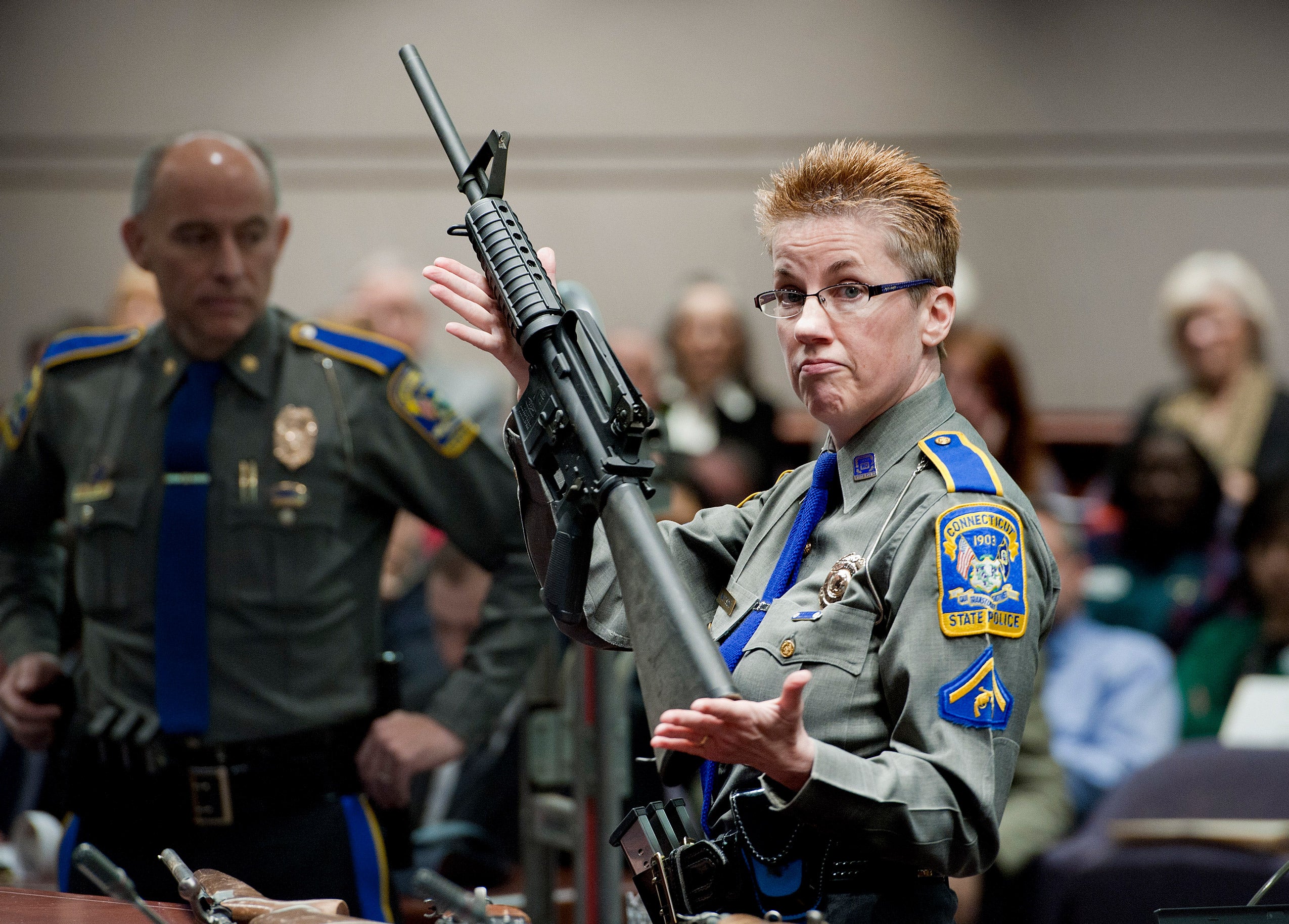 Police officer displaying a rifle in a courtroom.