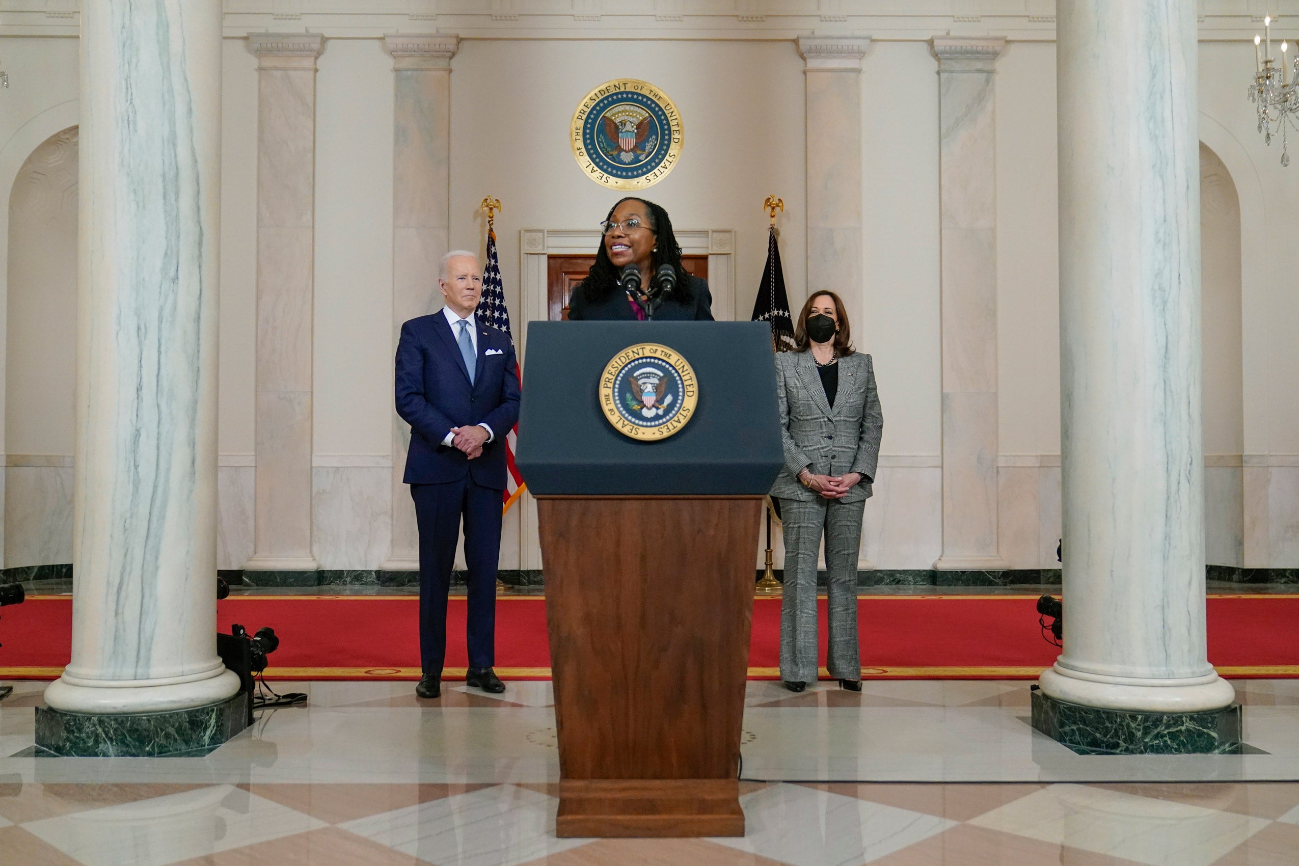 Judge Ketanji Brown Jackson speaks and a podium. President Biden and Vice President Harris standing behind her.