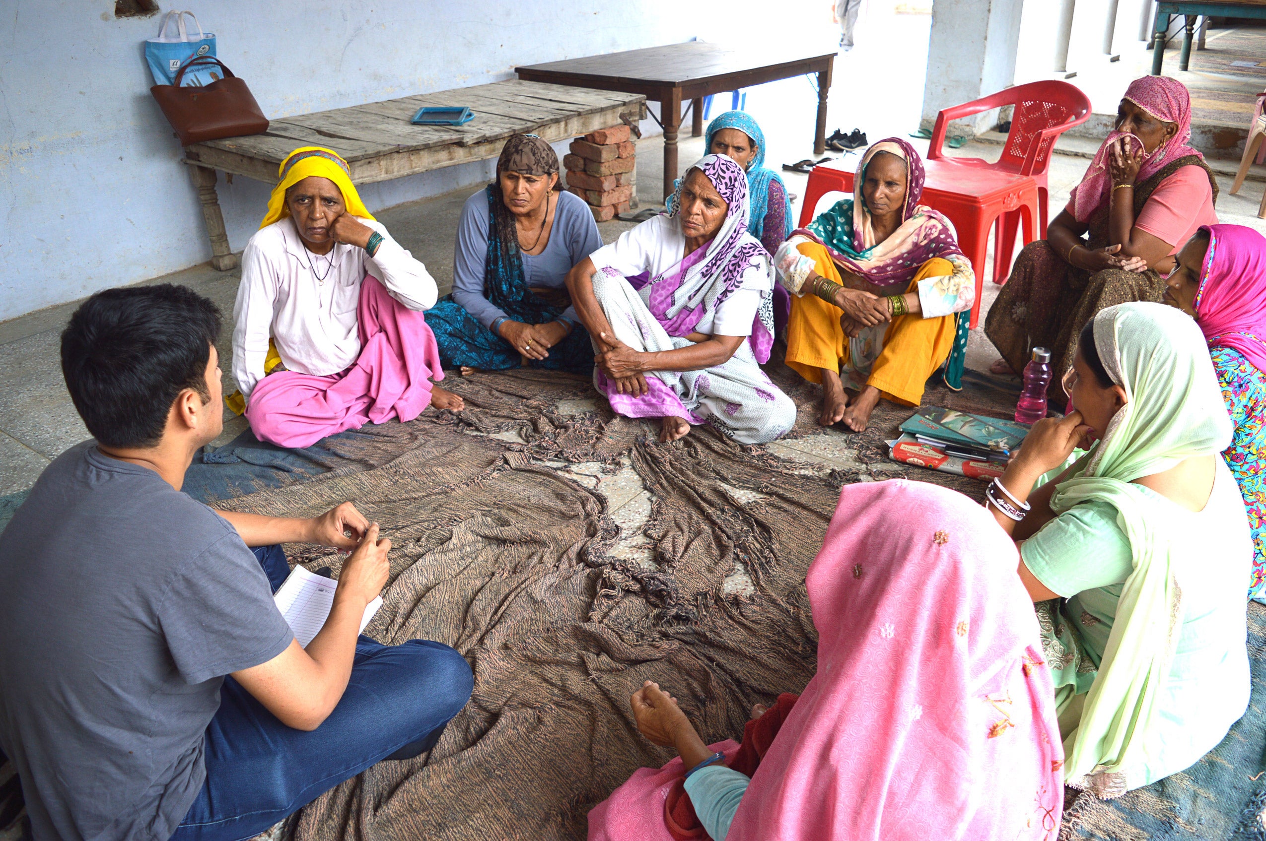 Aditya Pai sitting in sand with 8 women in headdresses sitting around him listening