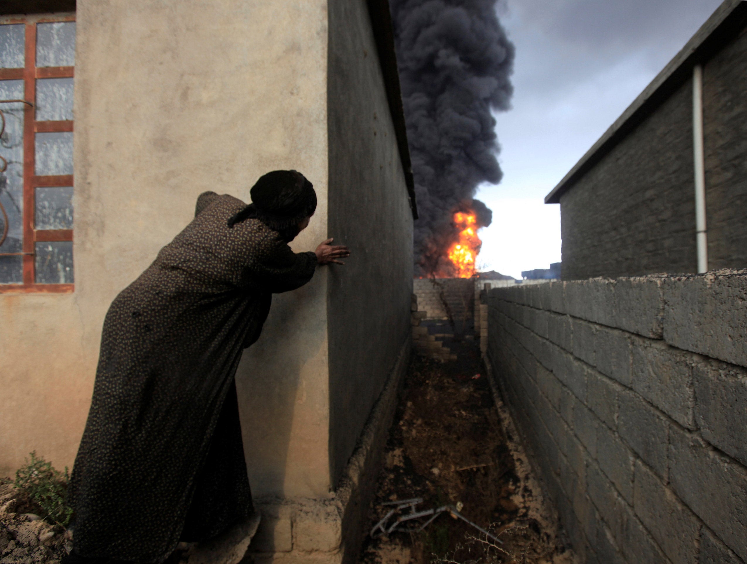 A woman looks at fire and smoke from oil wells set ablaze
