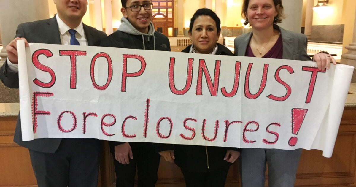 People holding sign that says "STOP UNJUST Forclosures!"