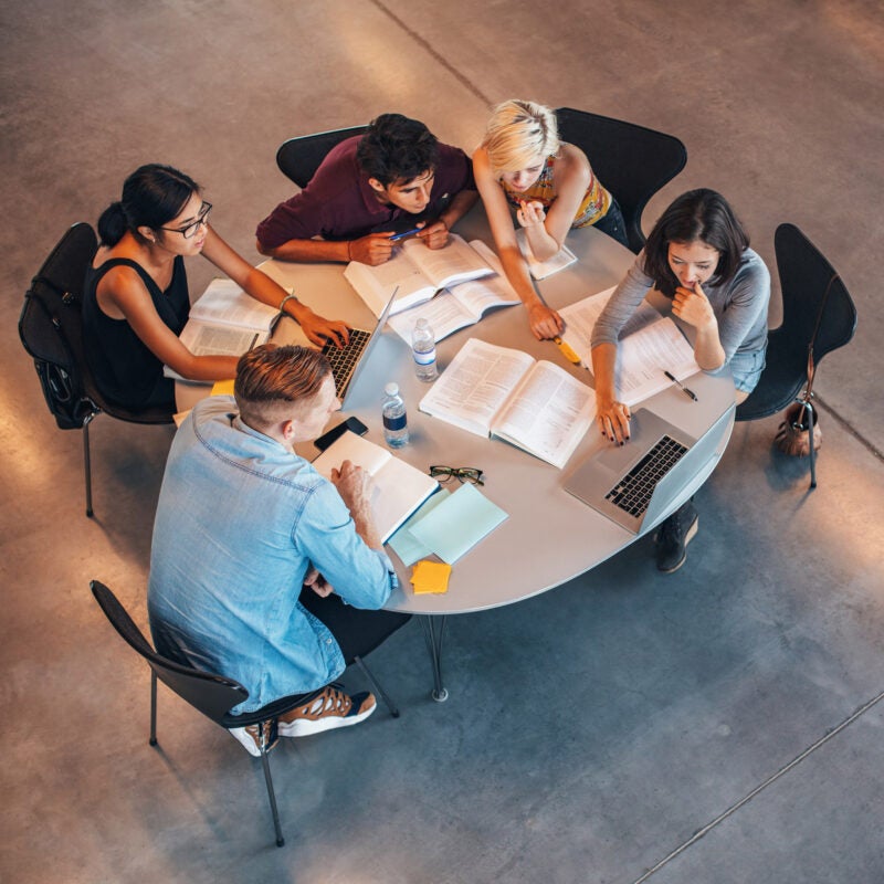 High angle shot of young people sitting at the table with books and laptops..