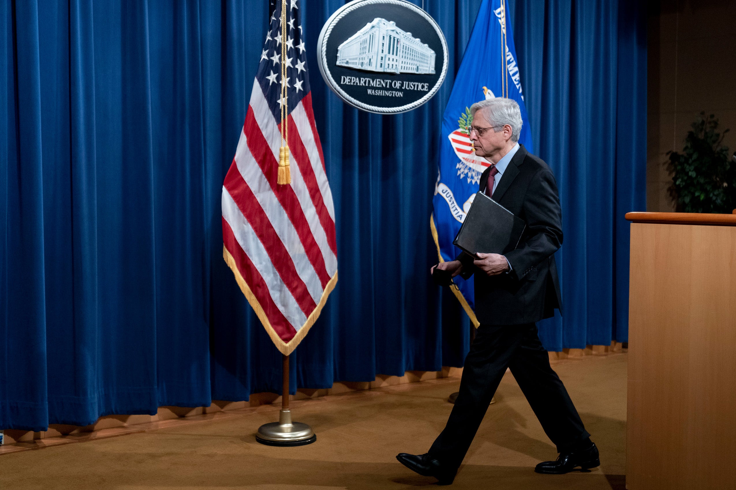 Man walking away from a podium by an American Flag and a sign that says Department of Justice Washington