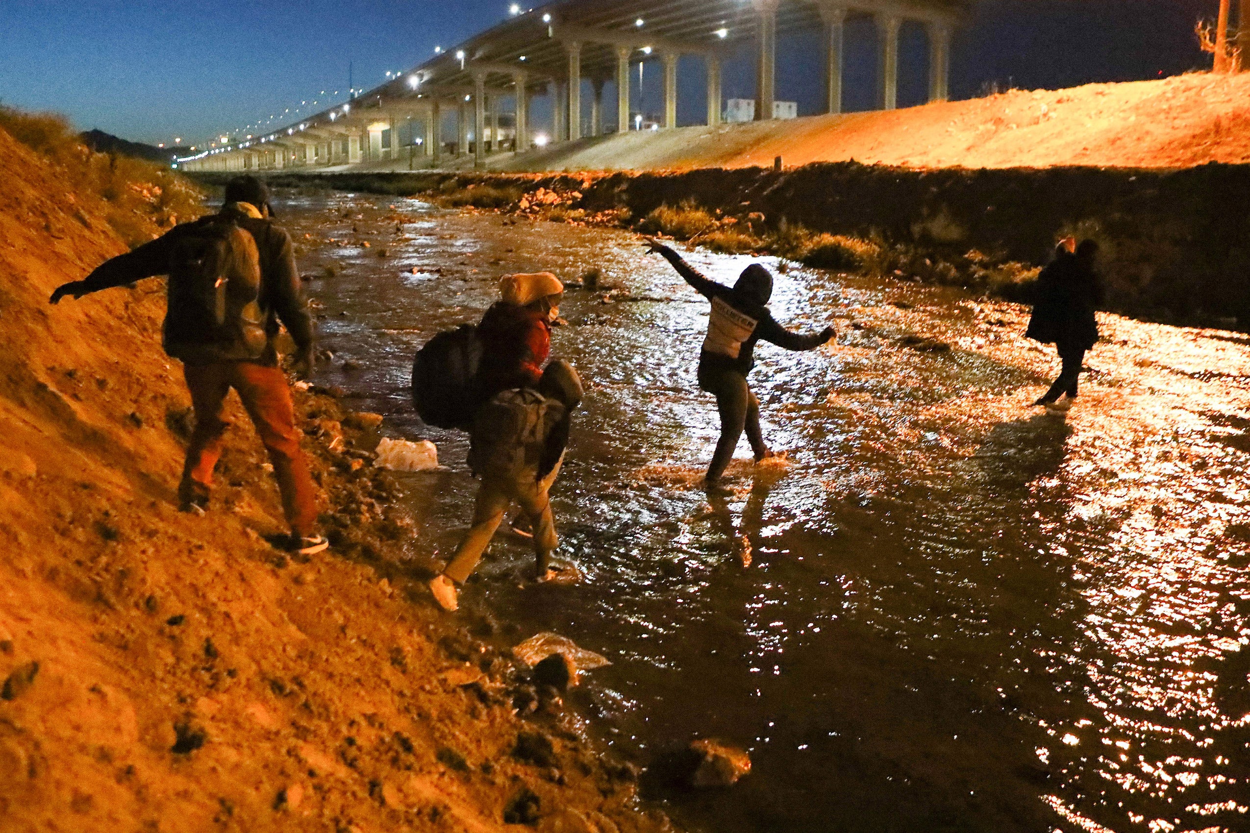 Four individuals wearing backpacks crossing over river at night