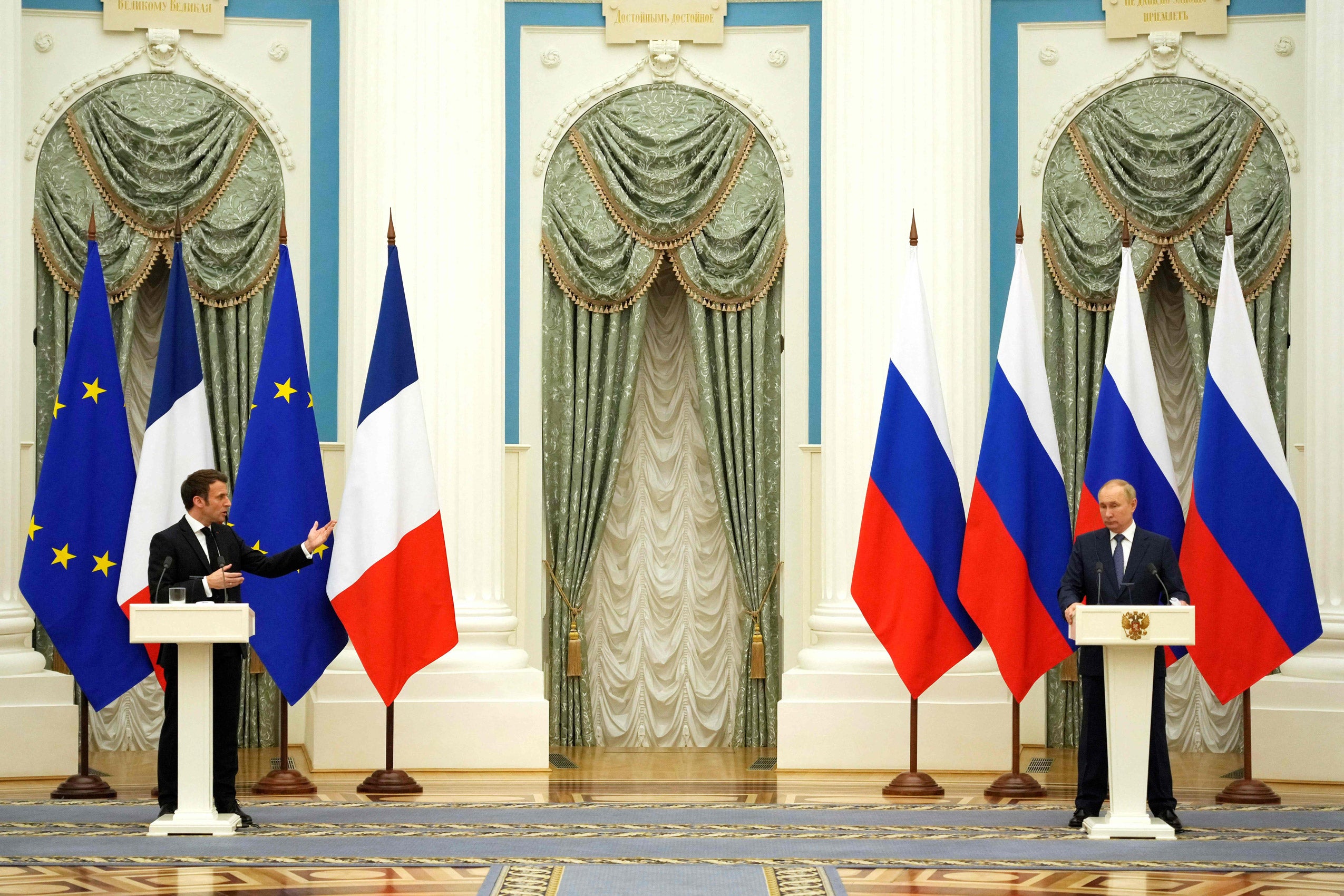 Two men speaking at white podiums with flags behind them