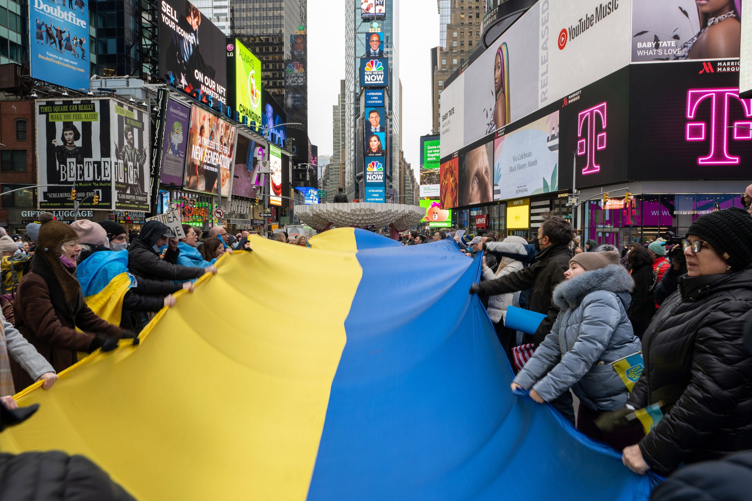 Crowd of people in New York City's Times Square carrying a large Ukranian flag