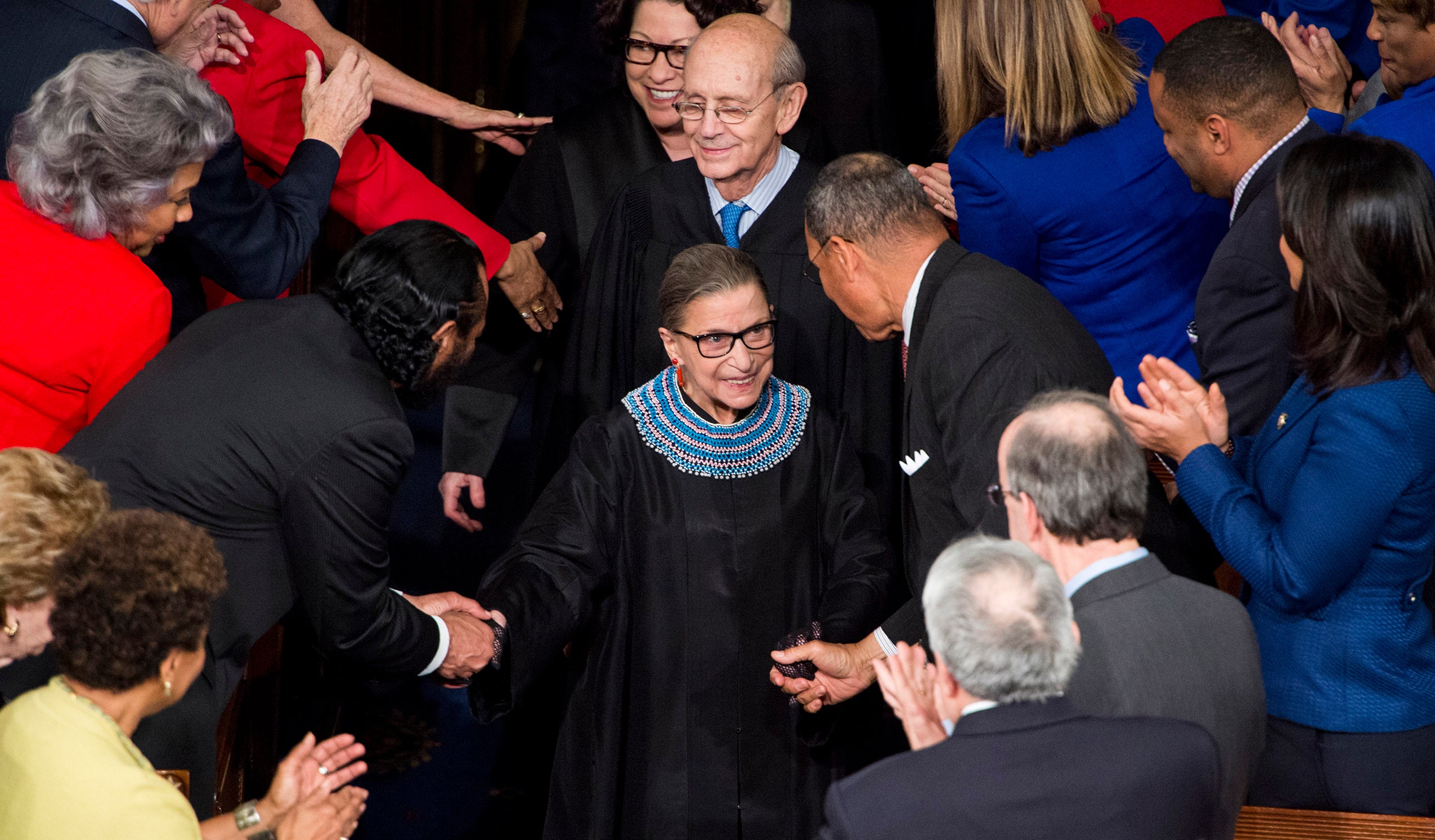Ruth Bader Ginsburg arriving at the State of The Union, wlaking down the aisle surrounded by justices and members of Congress.