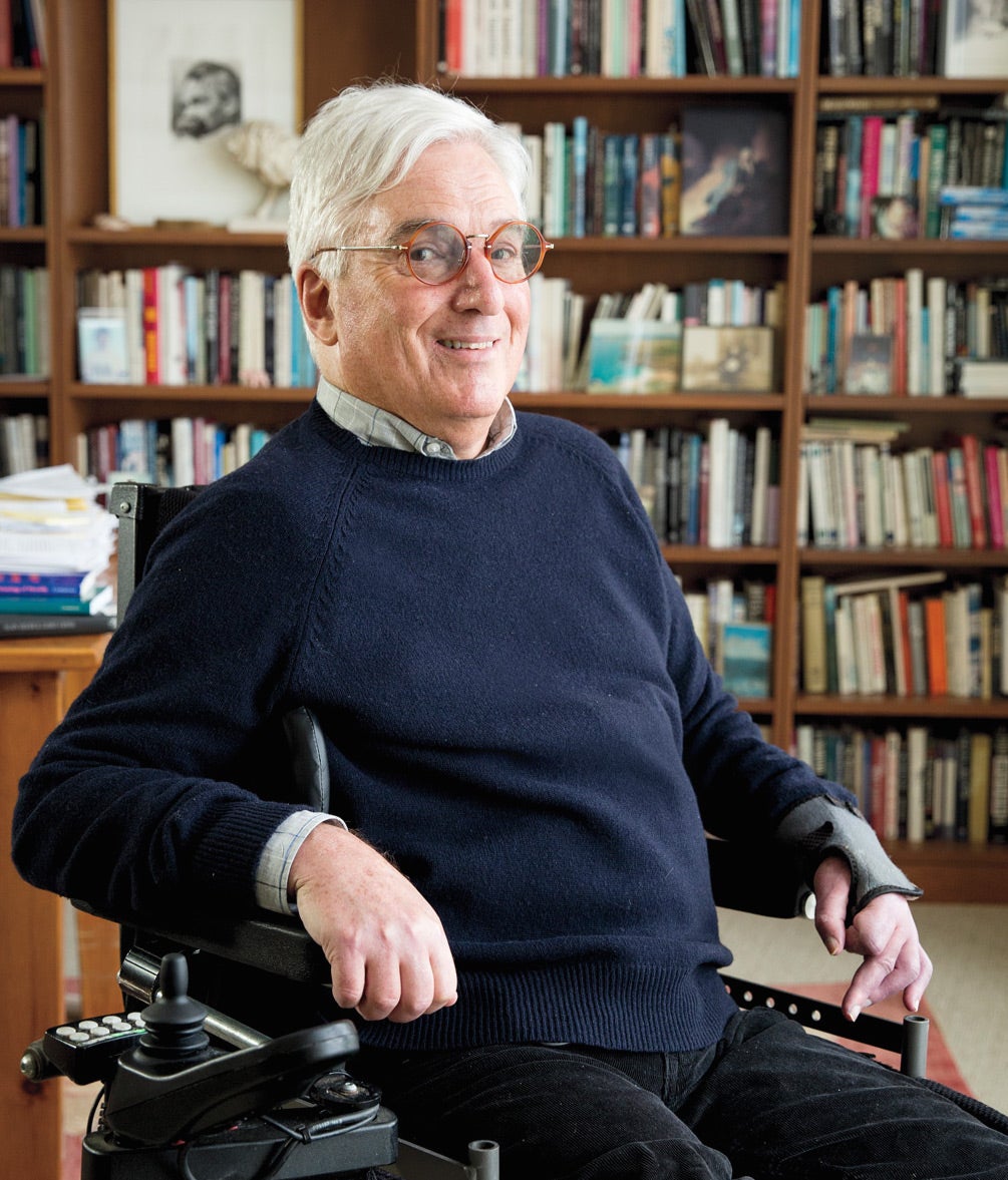 Professor Richard Parker sitting in an electric wheelchair smiling in front of a bookcase of books