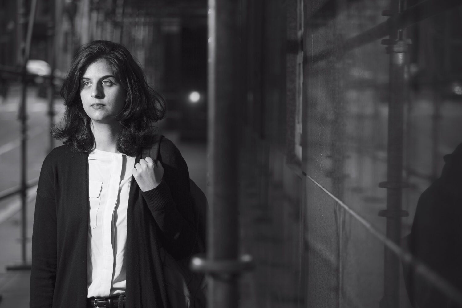 A woman holding a backpack walking under building rafting at night