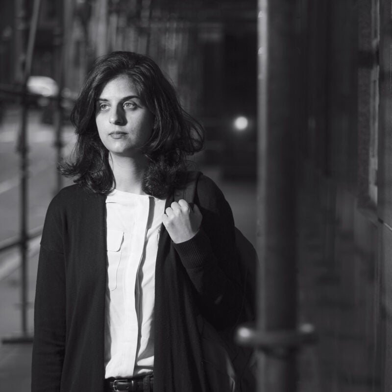 A woman holding a backpack walking under building rafting at night
